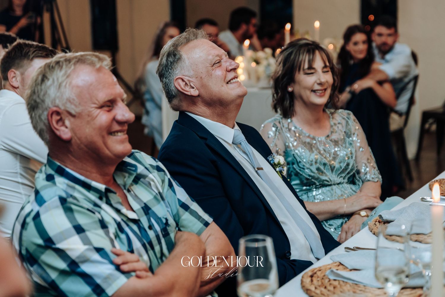 Wedding guests share laughter during reception dinner at decorated indoor venue.