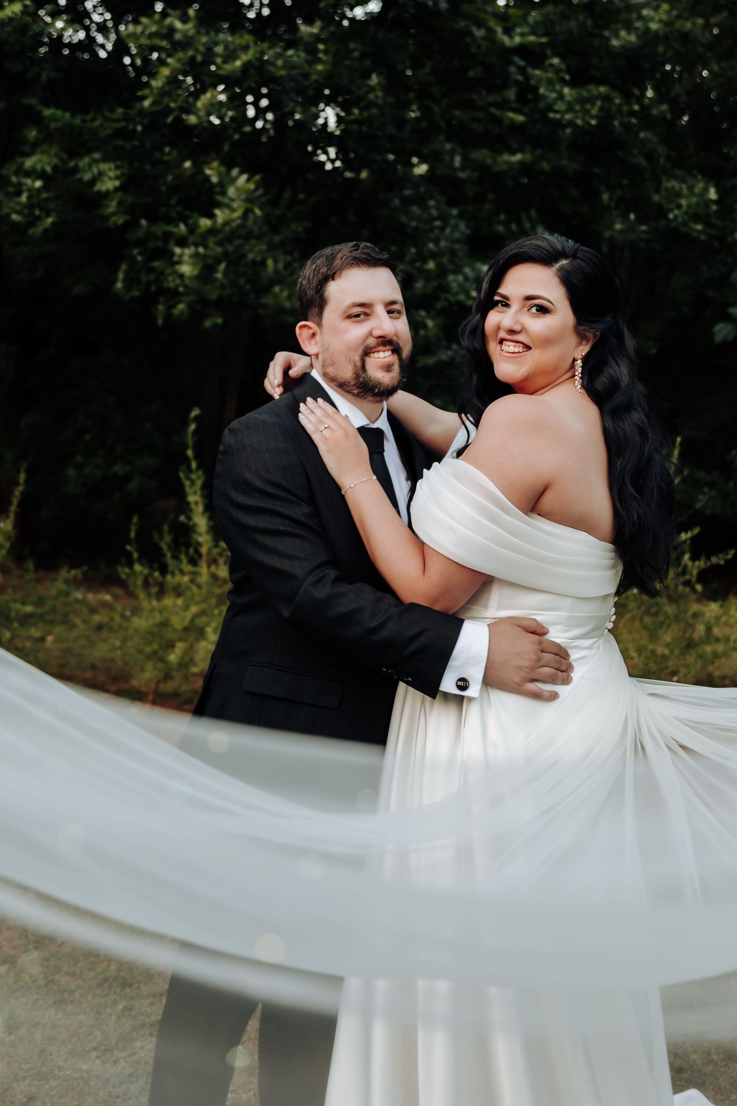 A romantic wedding couple embraces outdoors while the bride's white dress flows in the breeze.