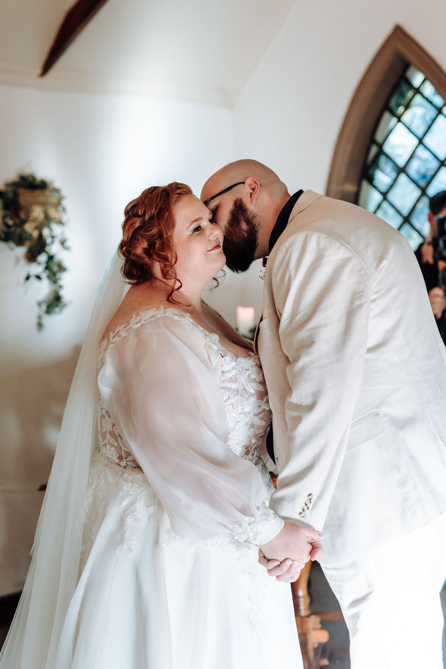 A romantic wedding couple shares intimate kisses in a series of elegant indoor portraits with natural lighting.