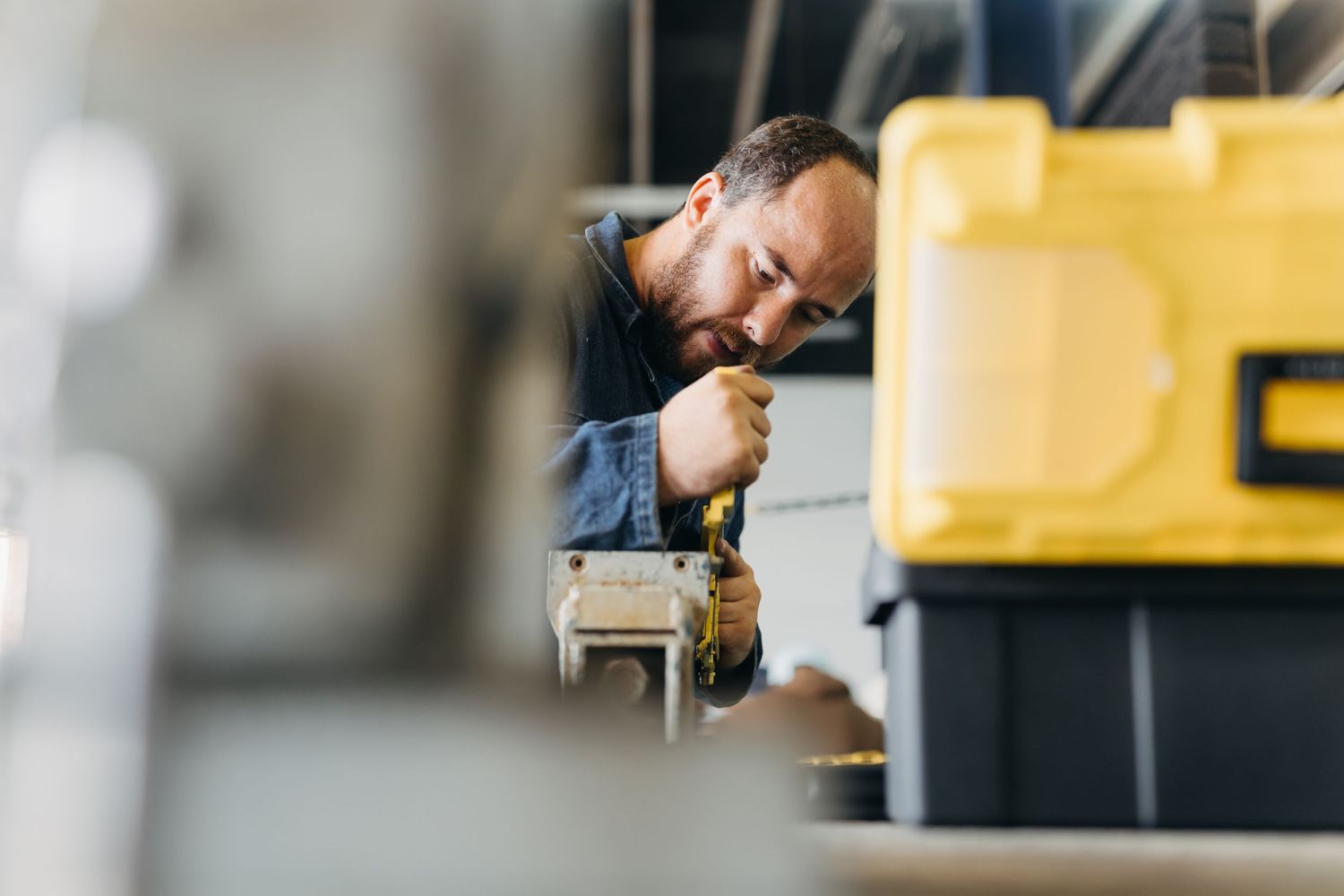 Person examining technical equipment in a laboratory with computer monitors and machinery visible in background.