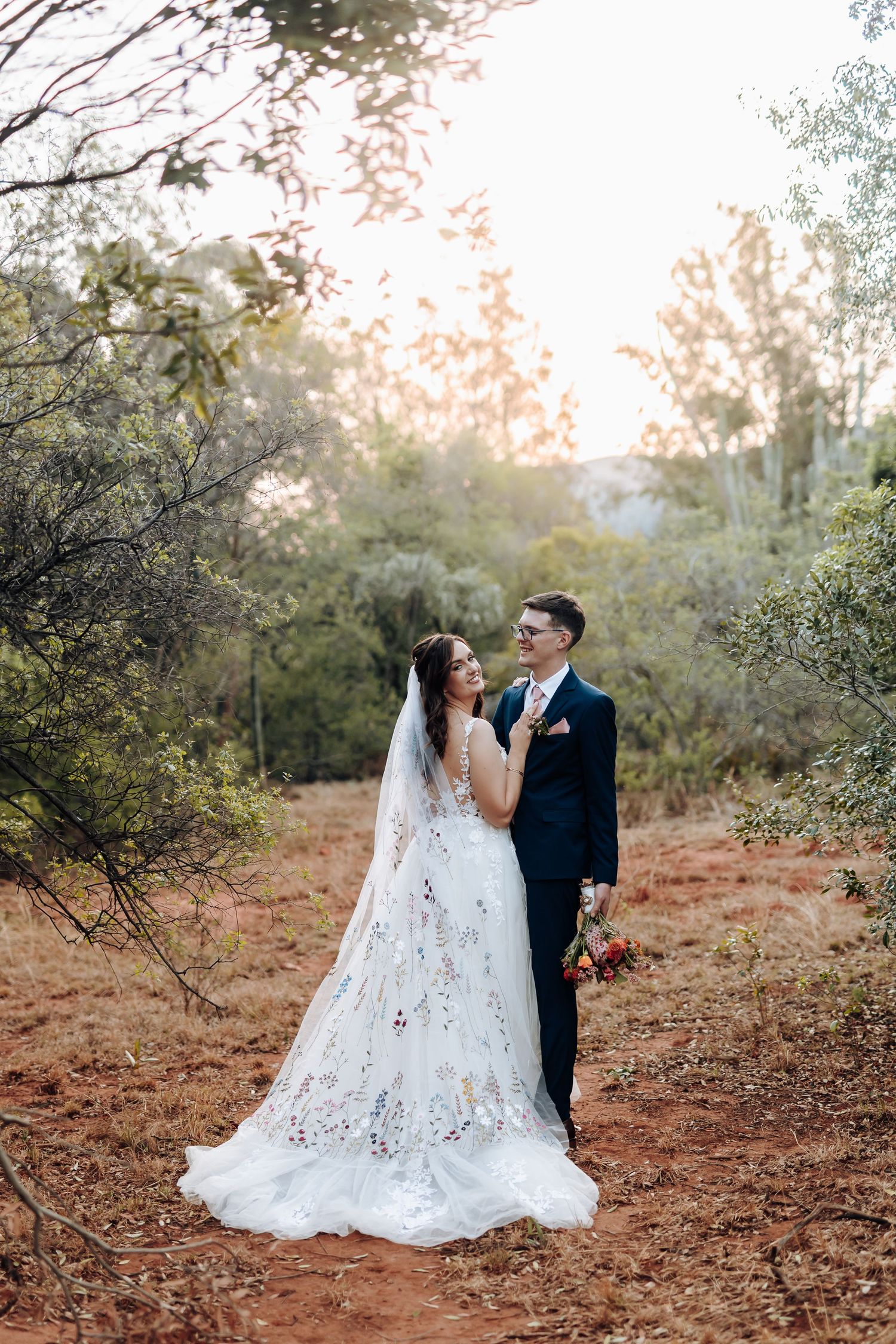 A romantic wedding couple poses in a natural outdoor setting with autumn foliage and soft lighting.