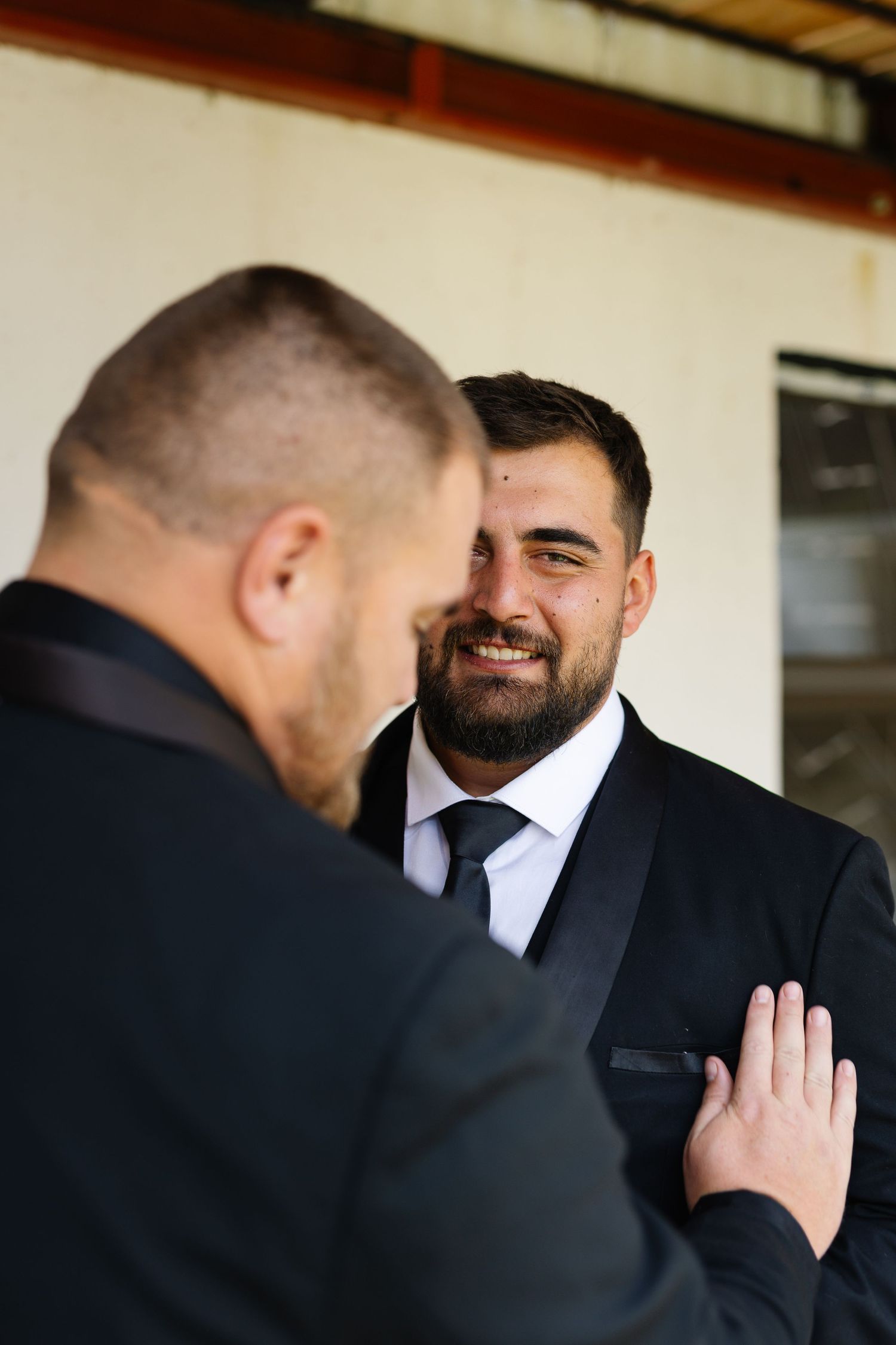 Two men in formal suits share a heartfelt moment during what appears to be a wedding celebration.