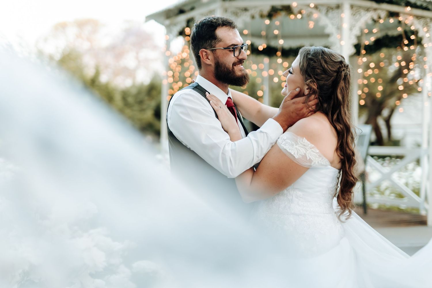 Intimate wedding portrait with couple embracing near a decorated gazebo.