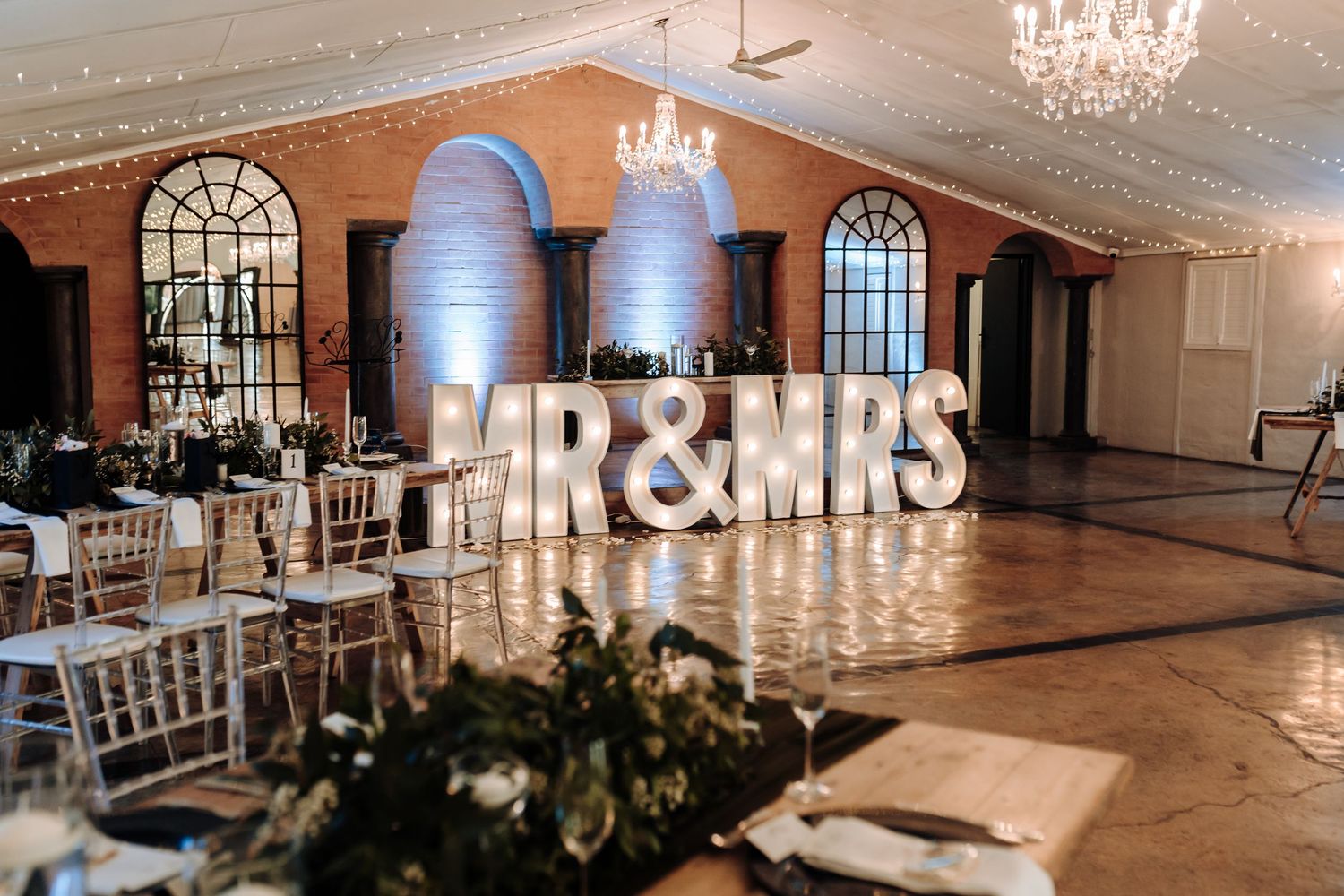 Wedding reception venue with illuminated 'MR & MRS' marquee letters and elegant chandeliers.