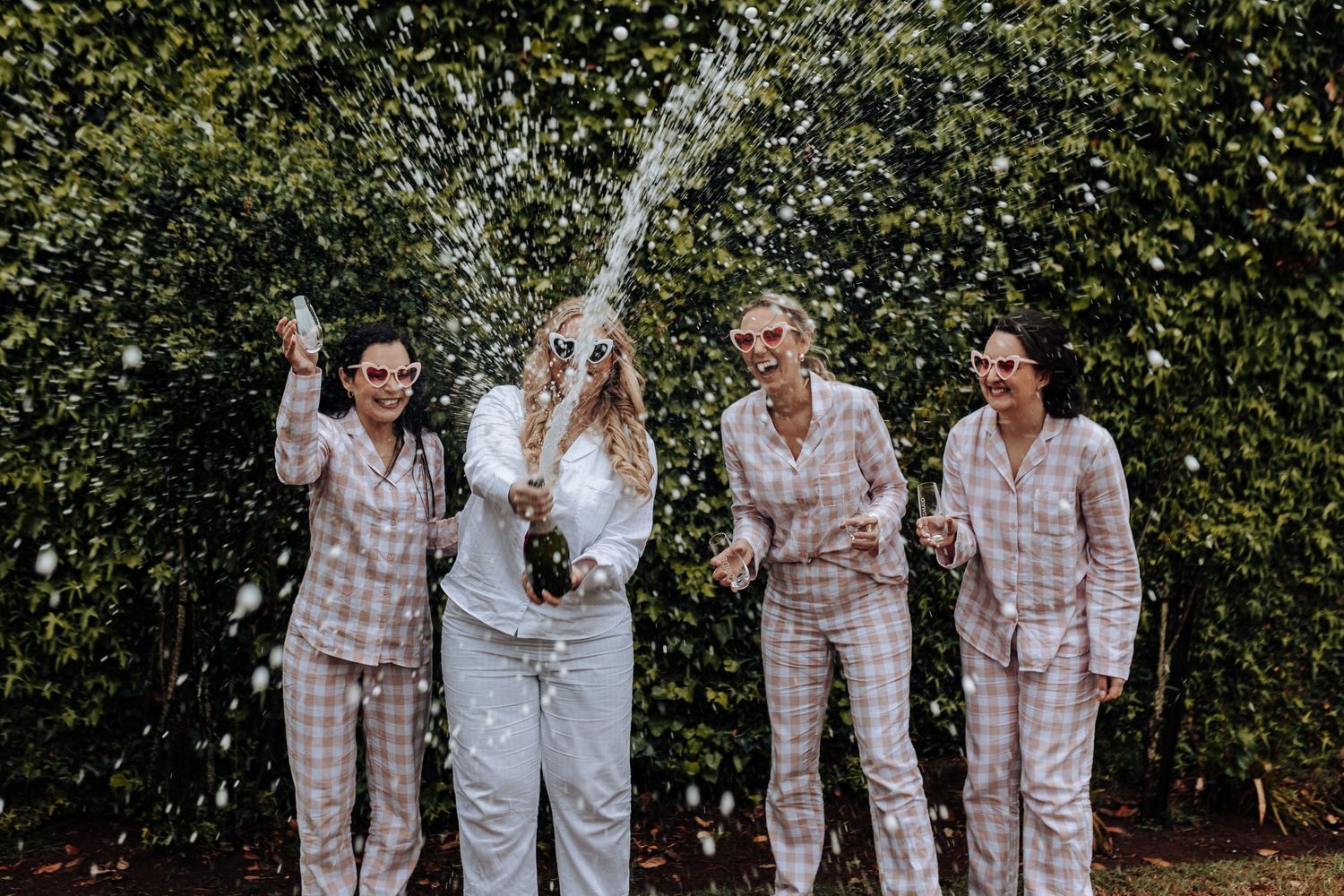 Friends in matching sleepwear celebrate by spraying champagne outdoors.