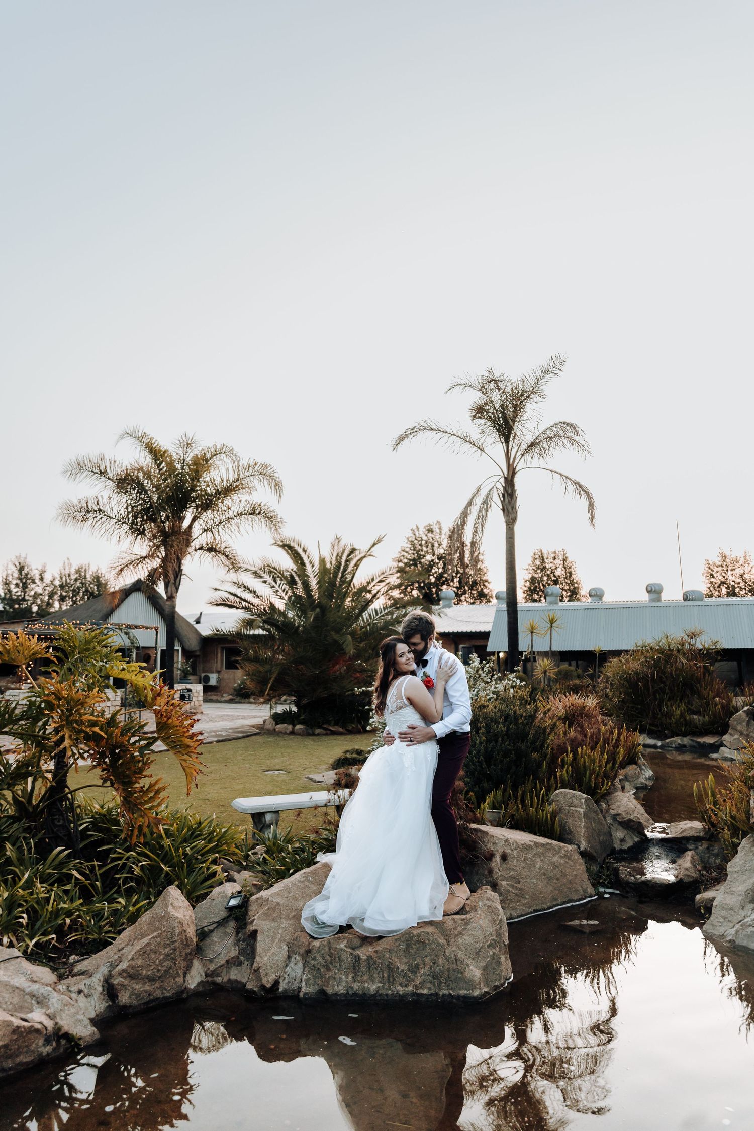Romantic wedding portrait captured on rocky water feature with tropical landscaping.