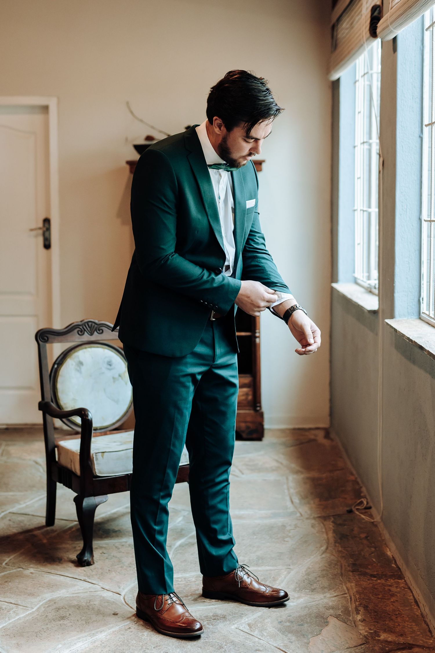 Full-length view of emerald green formal suit with brown leather shoes in elegant interior setting.