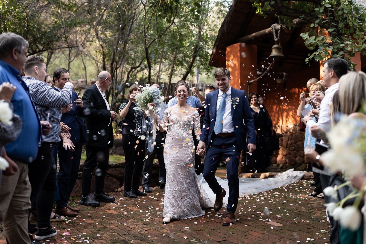 Guests shower newlyweds with confetti during outdoor garden wedding recessional.
