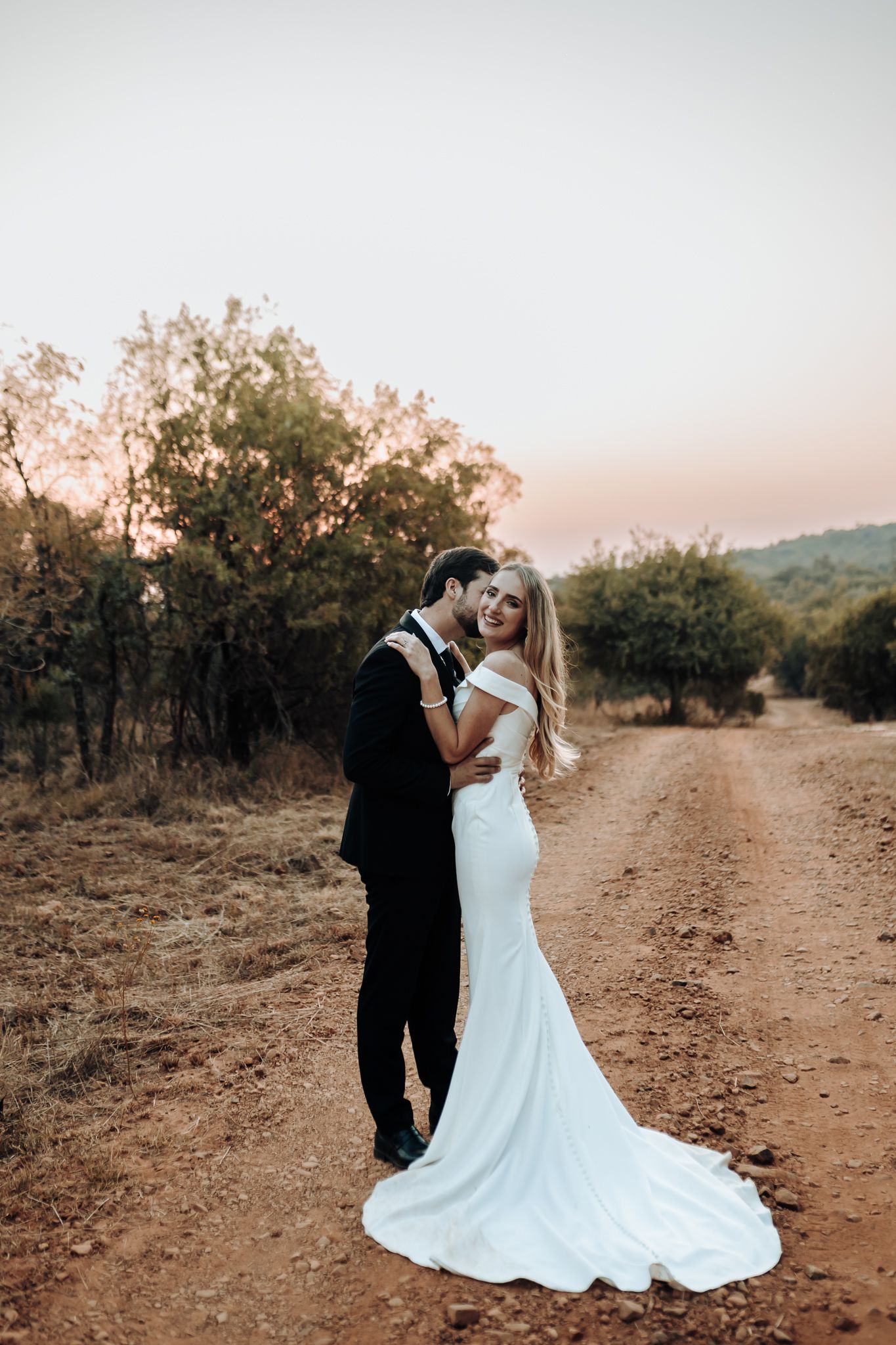 A romantic wedding photo on a rustic dirt road with a flowing white dress train.