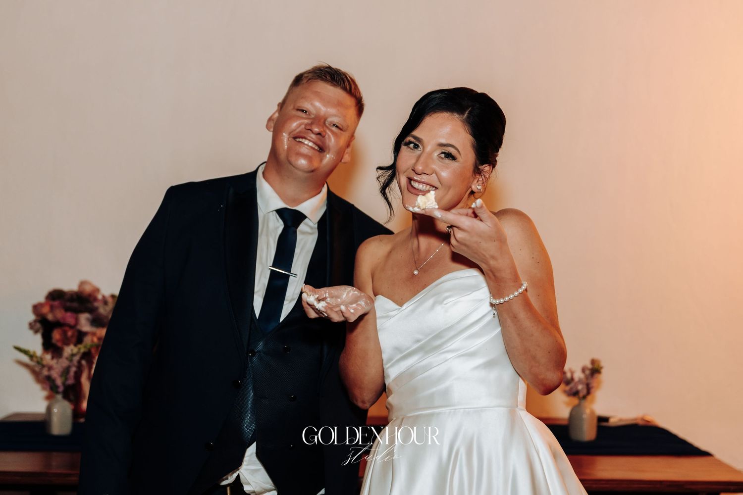 Happy newlyweds cutting wedding cake together, laughing and celebrating at their reception.