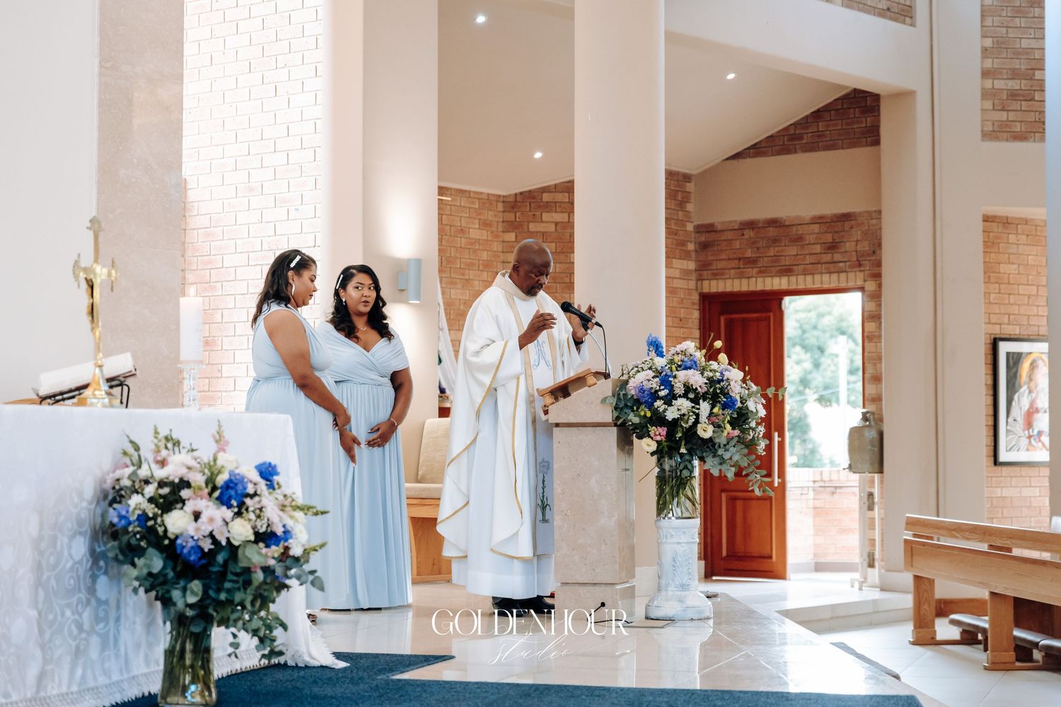 Wedding ceremony in progress at a modern church with brick walls and floral arrangements.