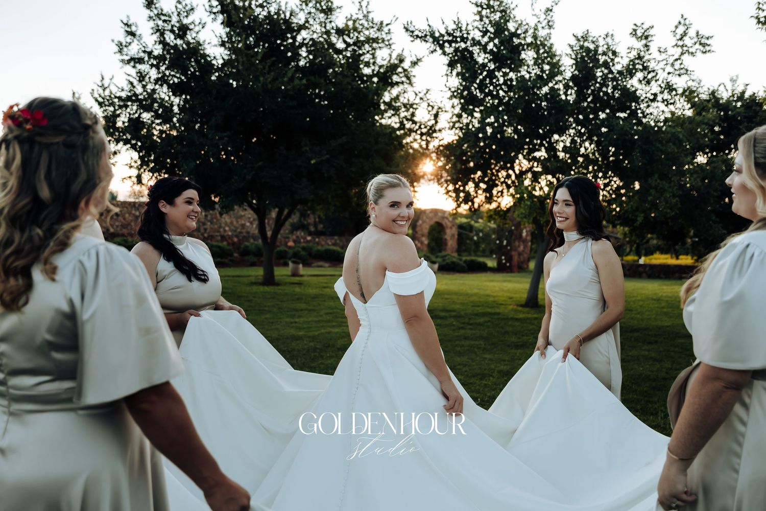 A group of people in white dresses dance together in an orchard during golden hour.
