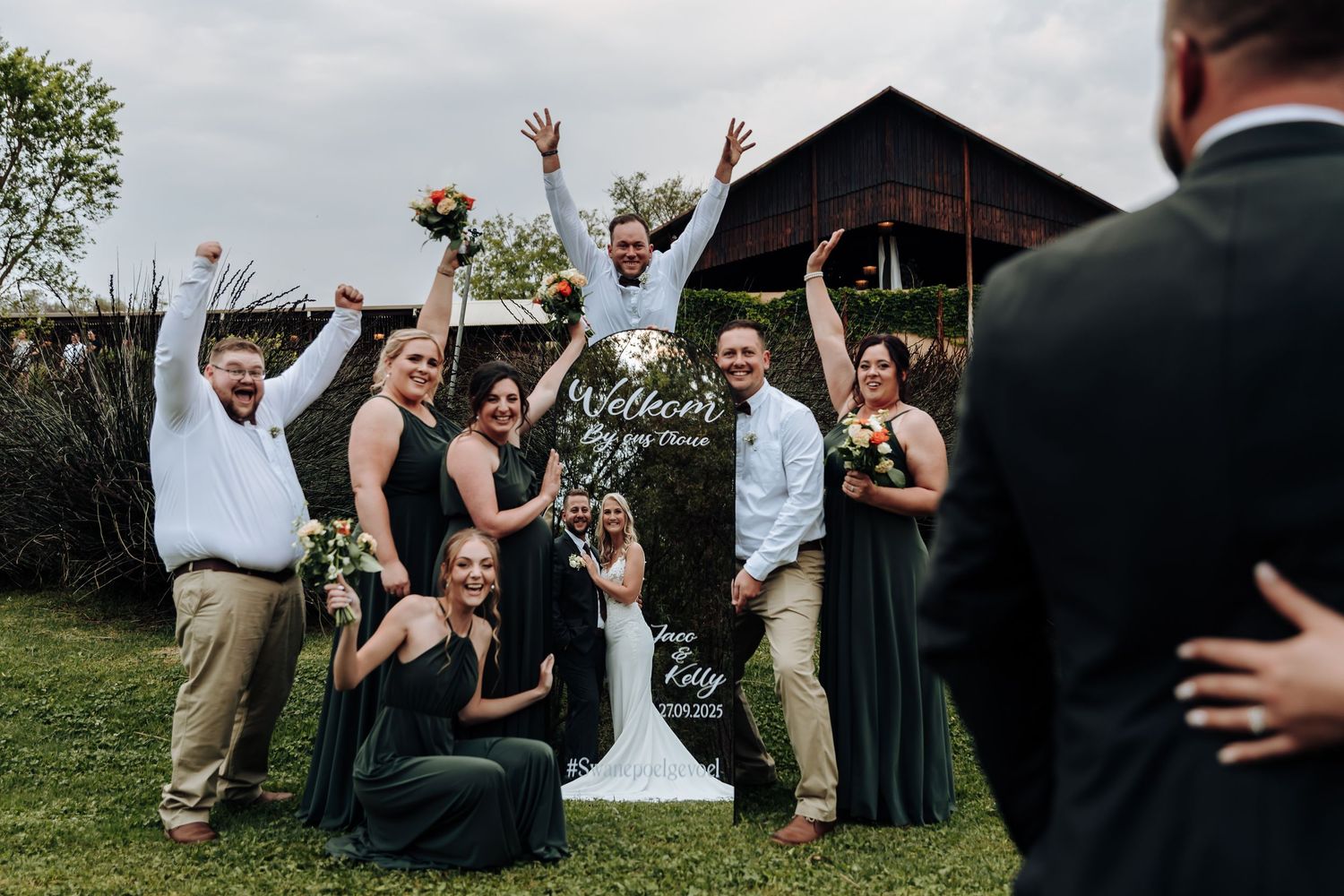 Wedding party jumps in celebration on a grassy lawn during an outdoor summer celebration.