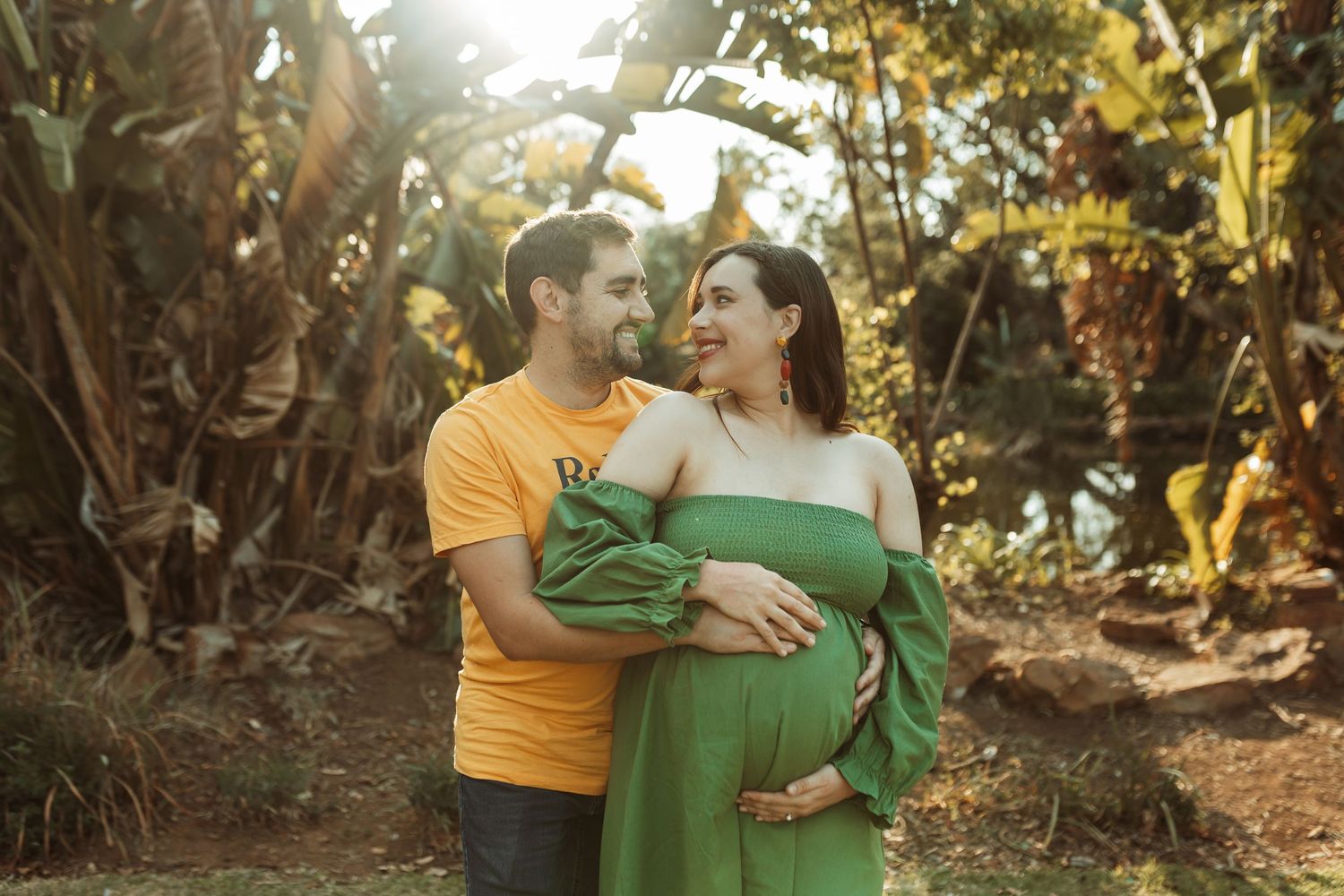 Loving couple in yellow and green outfits share affectionate moments while walking through a sunlit garden path.