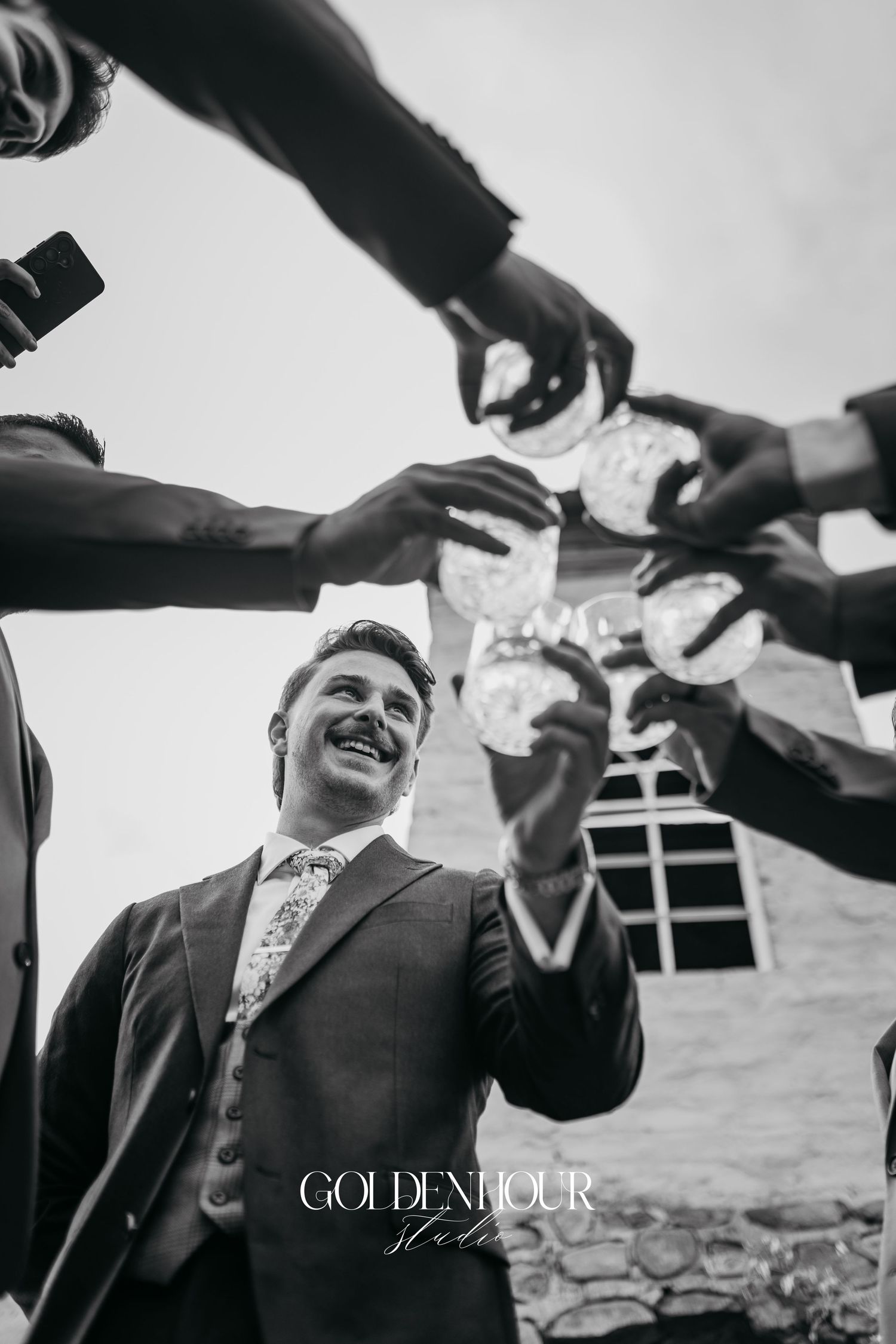 Black and white photo of groomsmen celebrating with outstretched hands in a joyful moment.
