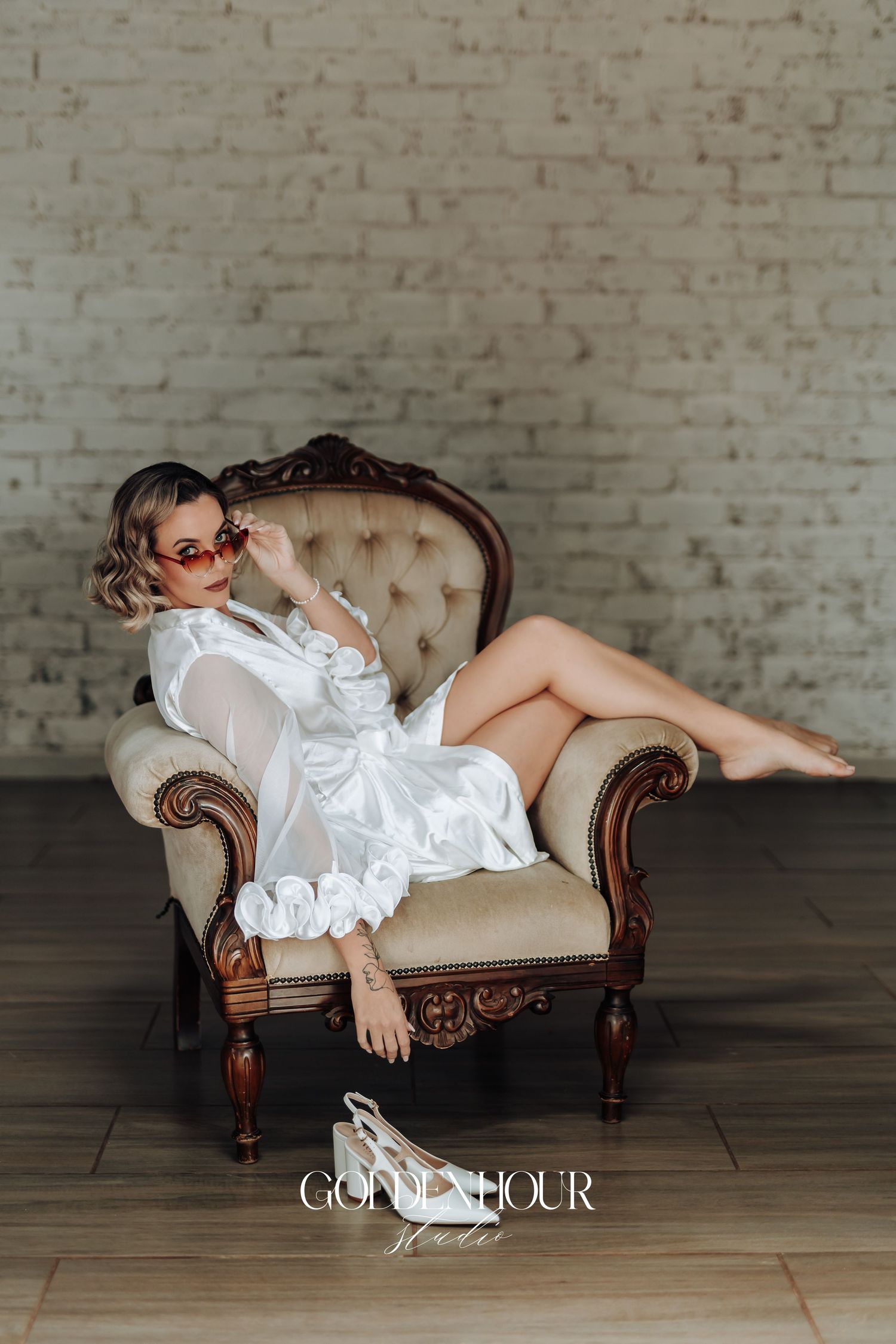 Person in white dress reclining on vintage tufted chaise lounge against brick wall.