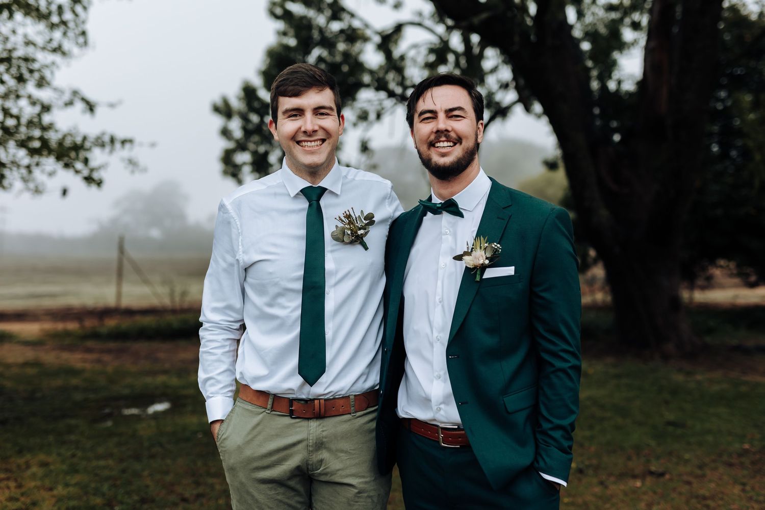 Wedding party members smile in coordinated emerald and white attire against natural backdrop.
