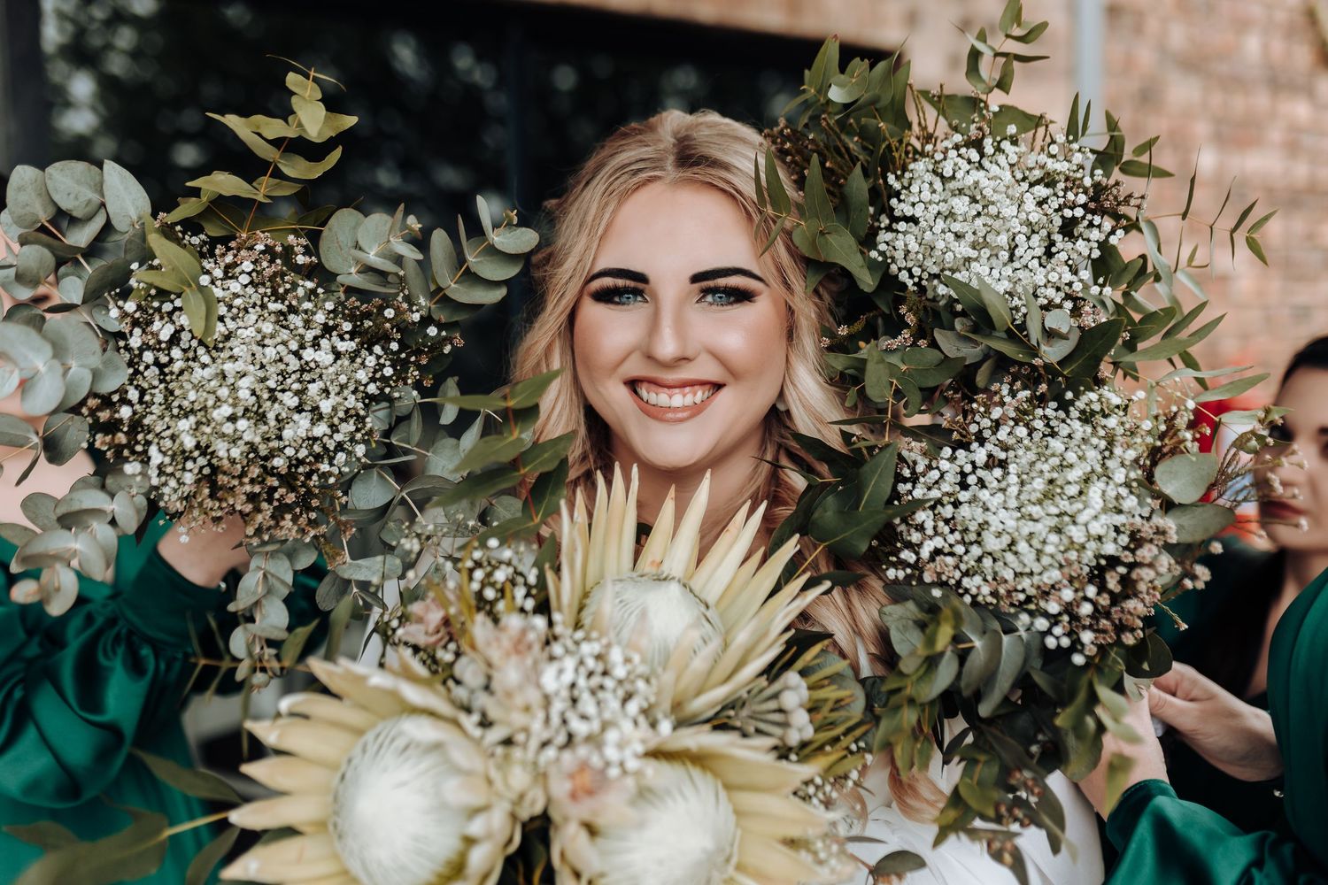 Close-up portrait of a radiant bride holding a white protea and baby's breath floral bouquet.