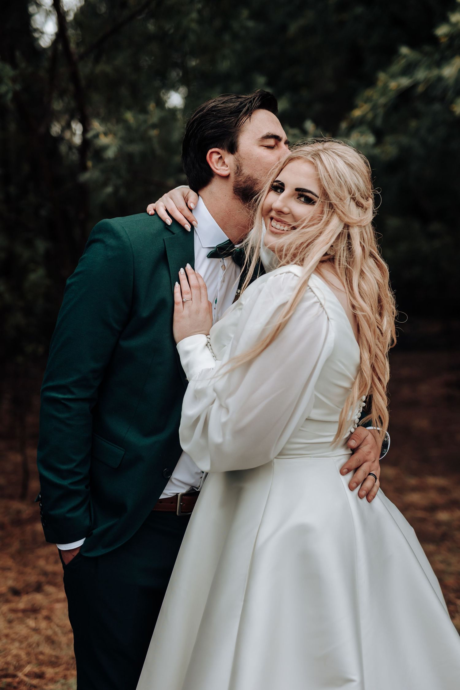 Intimate wedding moment captured as groom in green suit whispers to smiling bride in white dress.