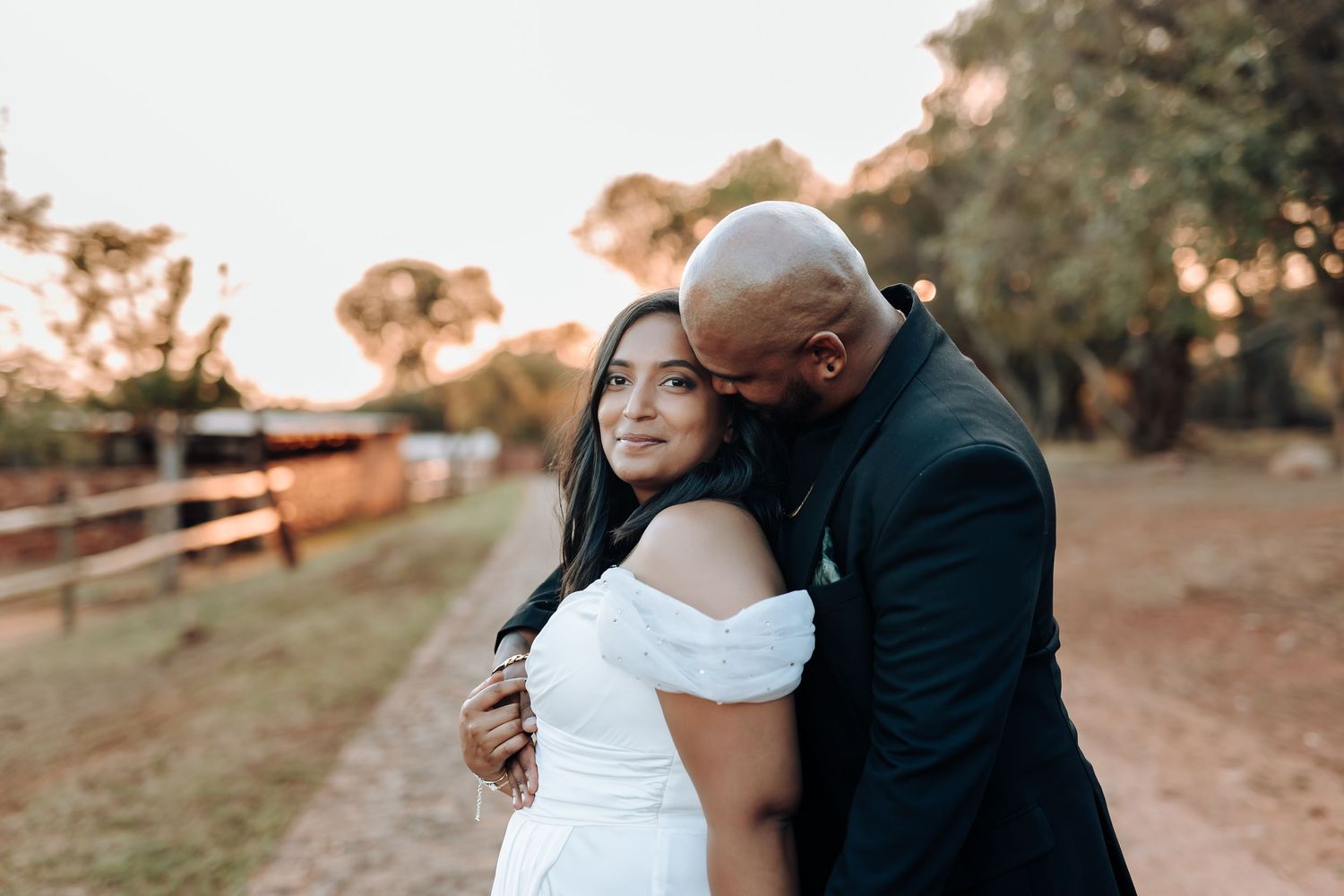 Sweet candid moment between couple during sunset wedding photoshoot near rustic fence.