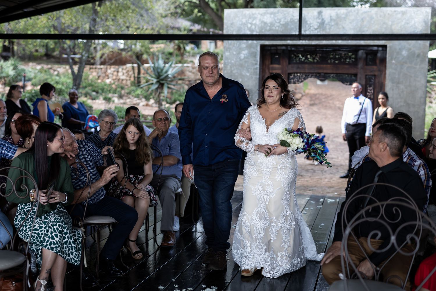 A bride and escort walk down the aisle during an outdoor wedding ceremony.