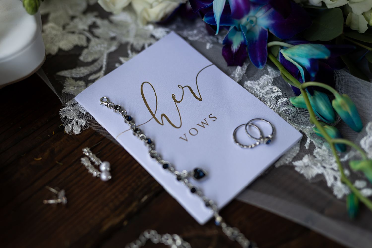 Wedding details with rings and vows book on dark wood surface with blue and white flowers.