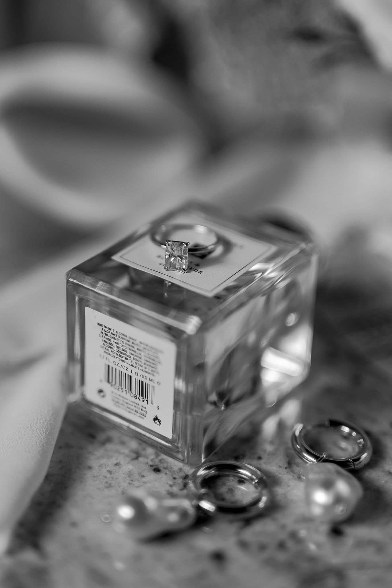 Diamond engagement ring perched on a glass cube with wedding bands scattered below in black and white.