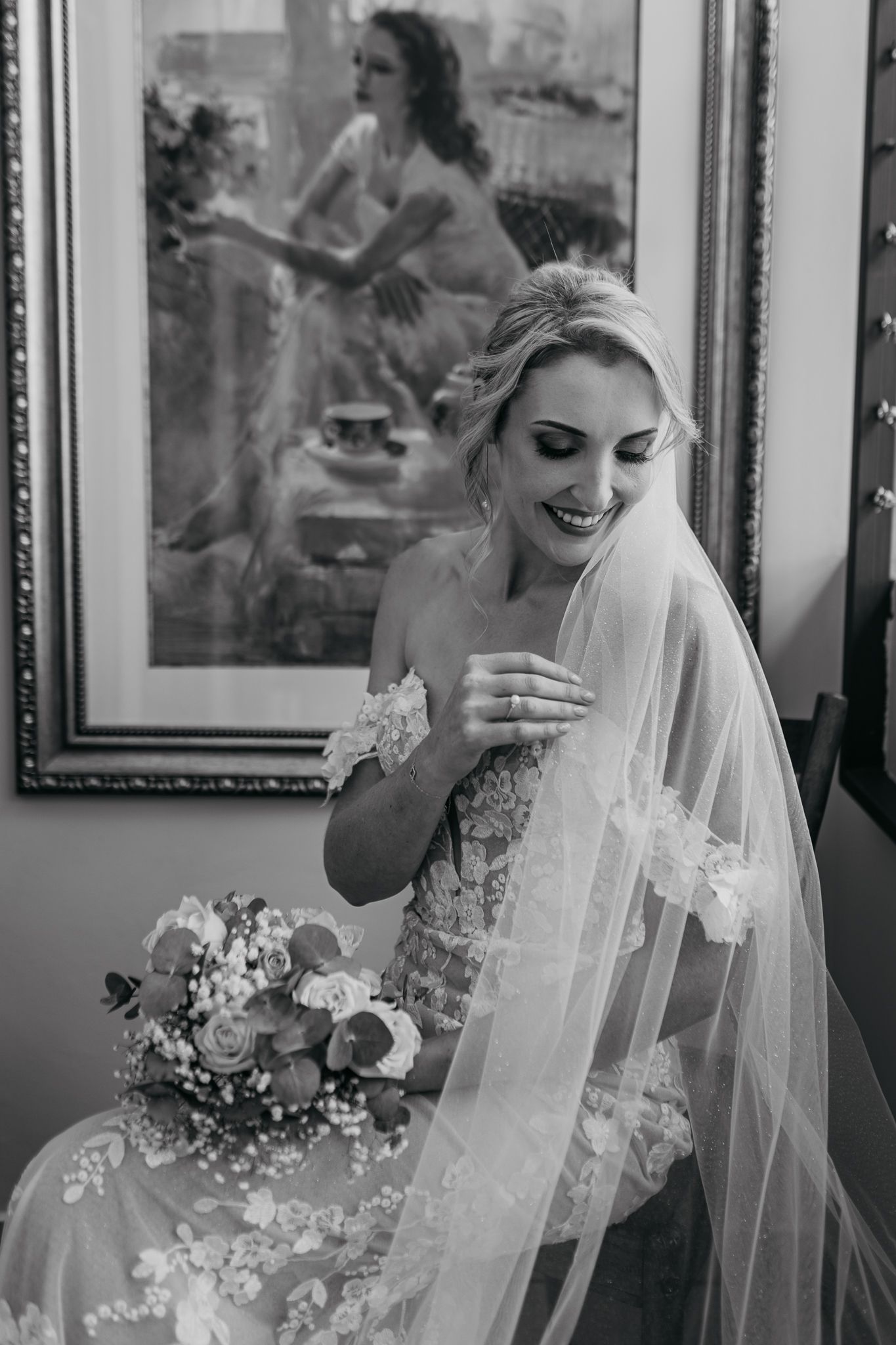 Black and white portrait of joyful bride laughing while seated with bouquet.