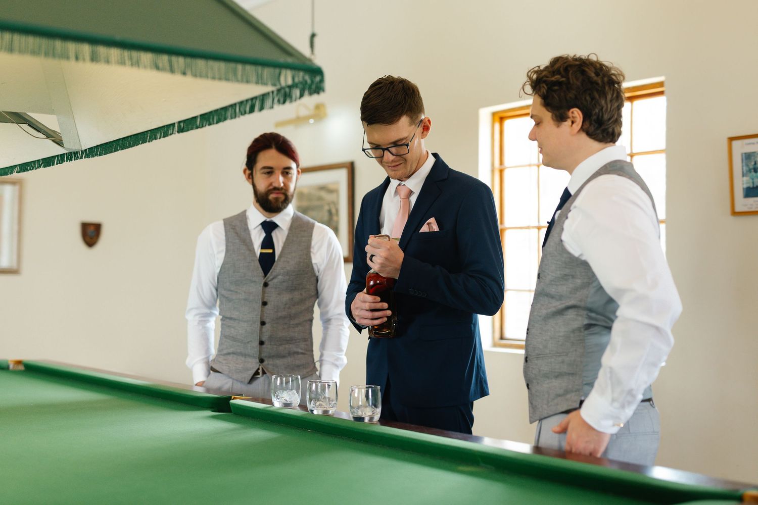 Wedding party members in formal attire gather around a bar counter during a celebration event.