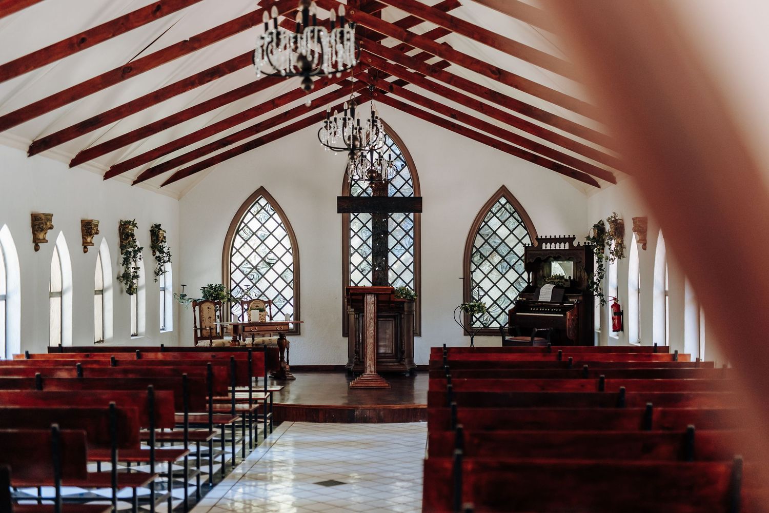 Interior view of a modern church sanctuary with white walls, wooden beams, and rows of red pews.