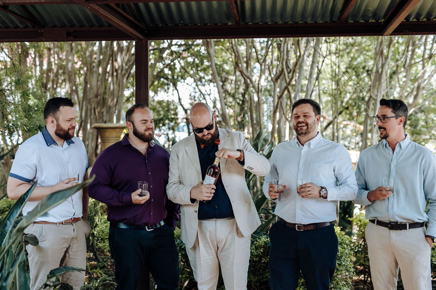 A group of people in formal attire gather outdoors for a celebratory toast with drinks at a social event.