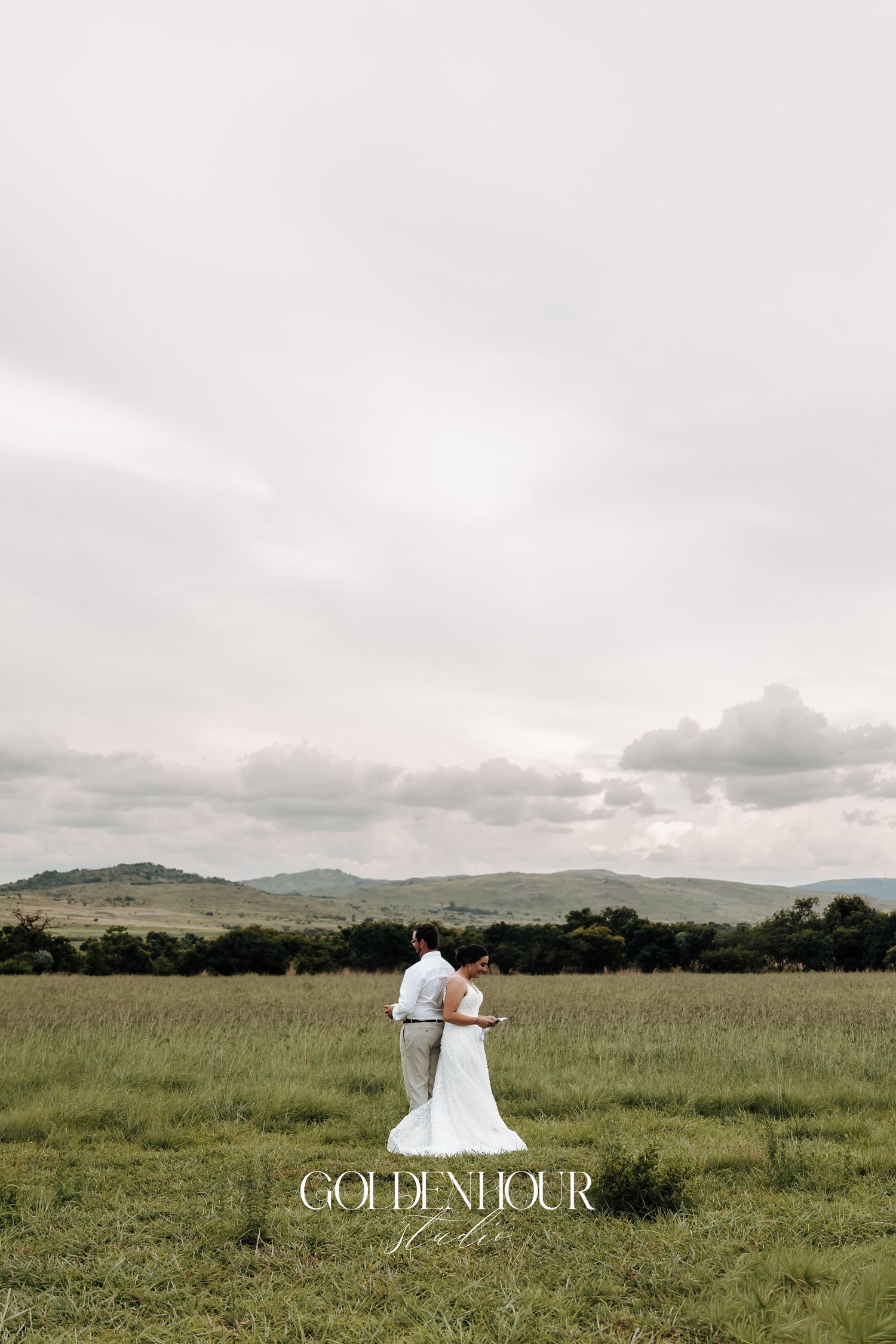 A romantic wedding scene unfolds in a serene meadow with rolling hills and dramatic cloudy skies.