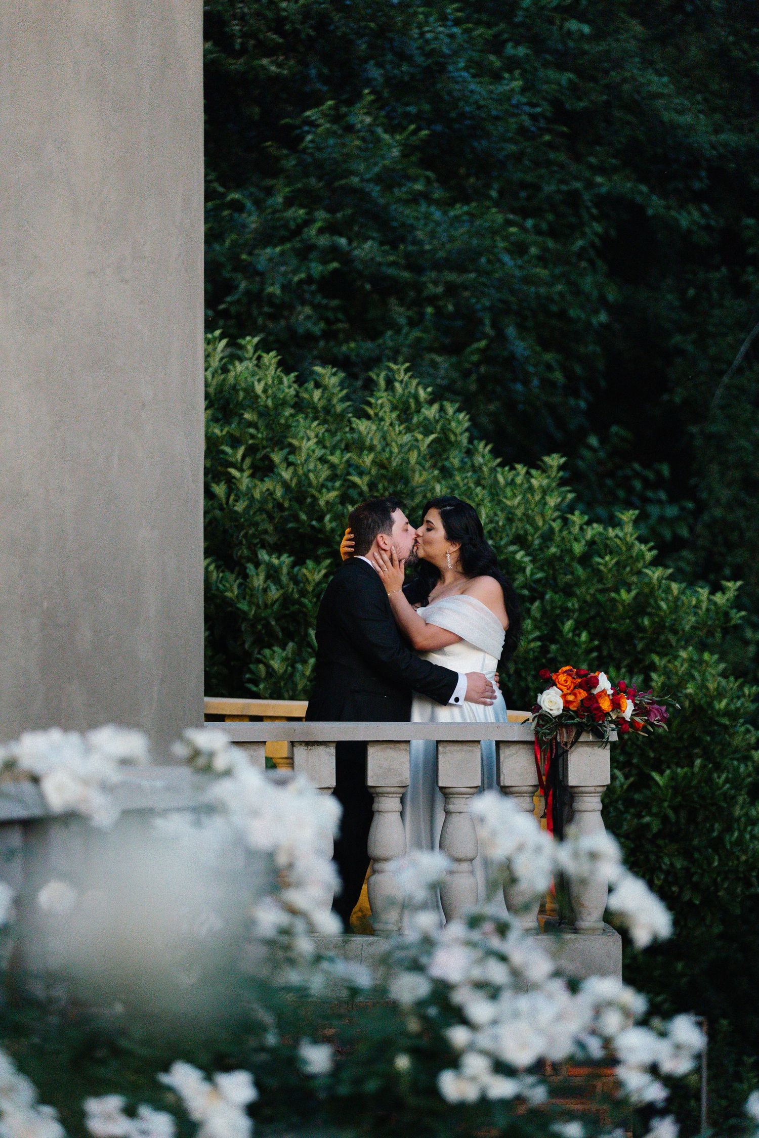 Romantic wedding couple moment captured through white flowers in foreground.
