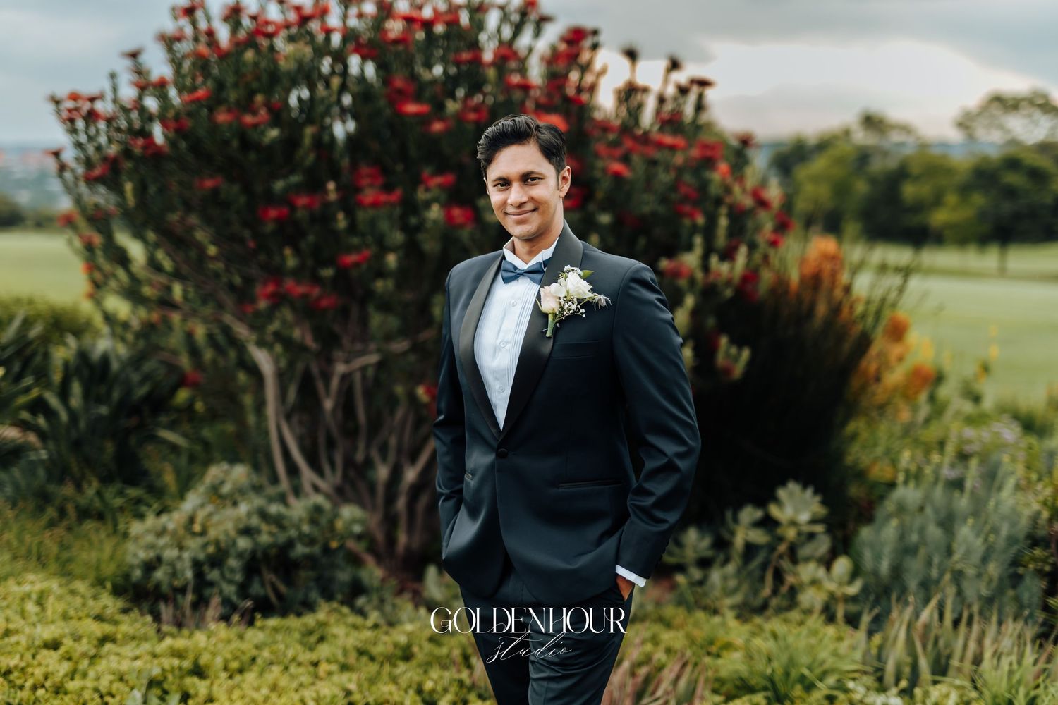 Wedding party poses outdoors near blooming red flower bush.