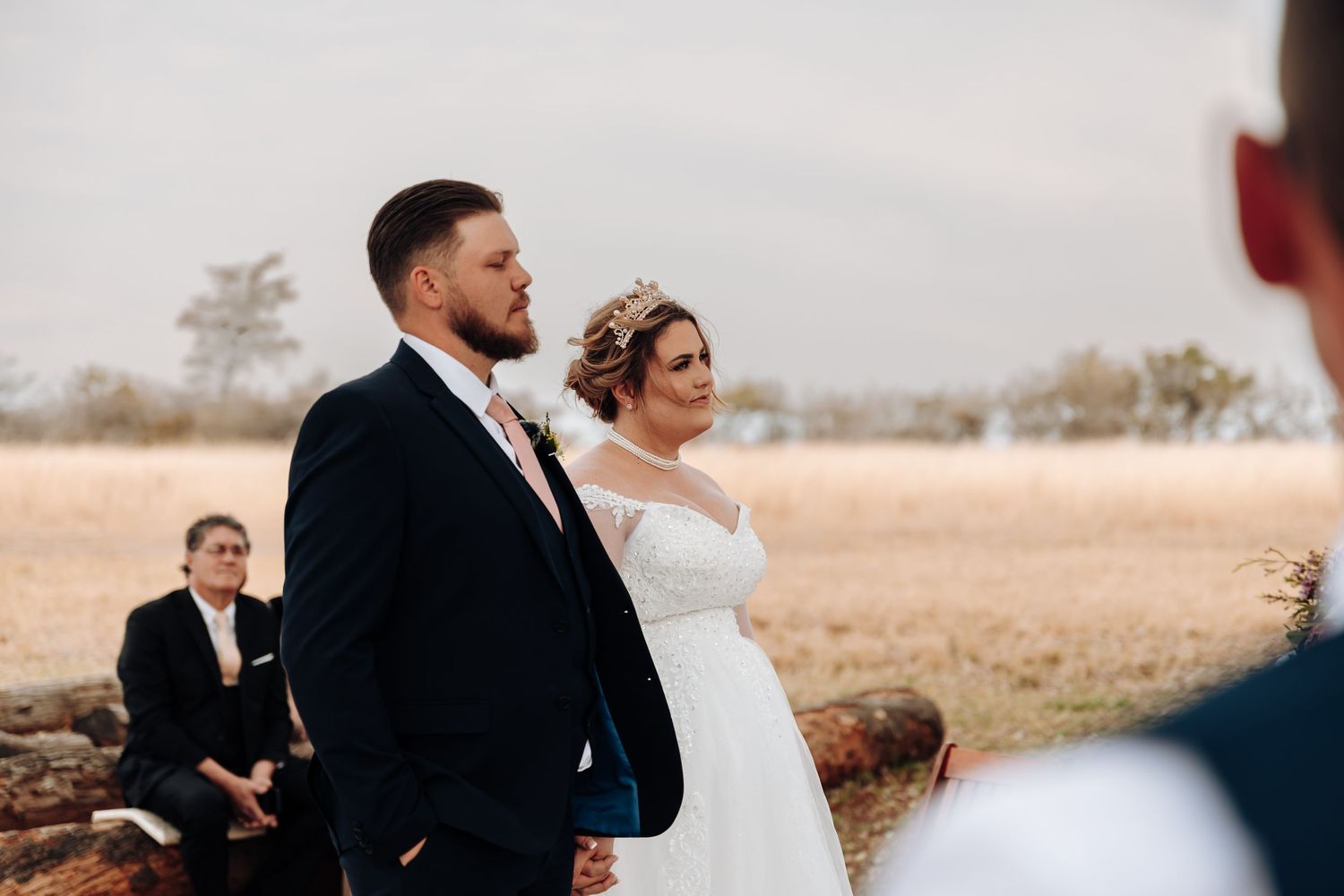 Newlywed couple shares an intimate dance in a scenic autumn field at sunset while photographer captures moment.