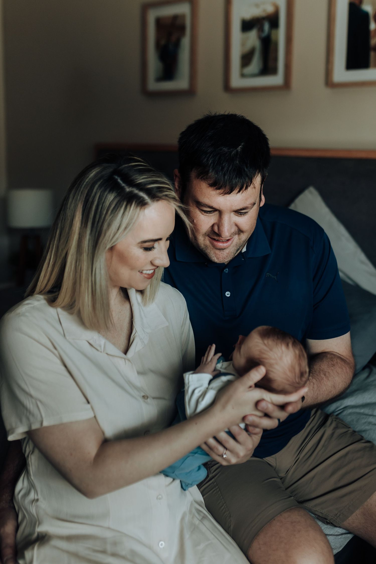 New parents share an intimate moment with their newborn baby in a cozy home setting by window light.
