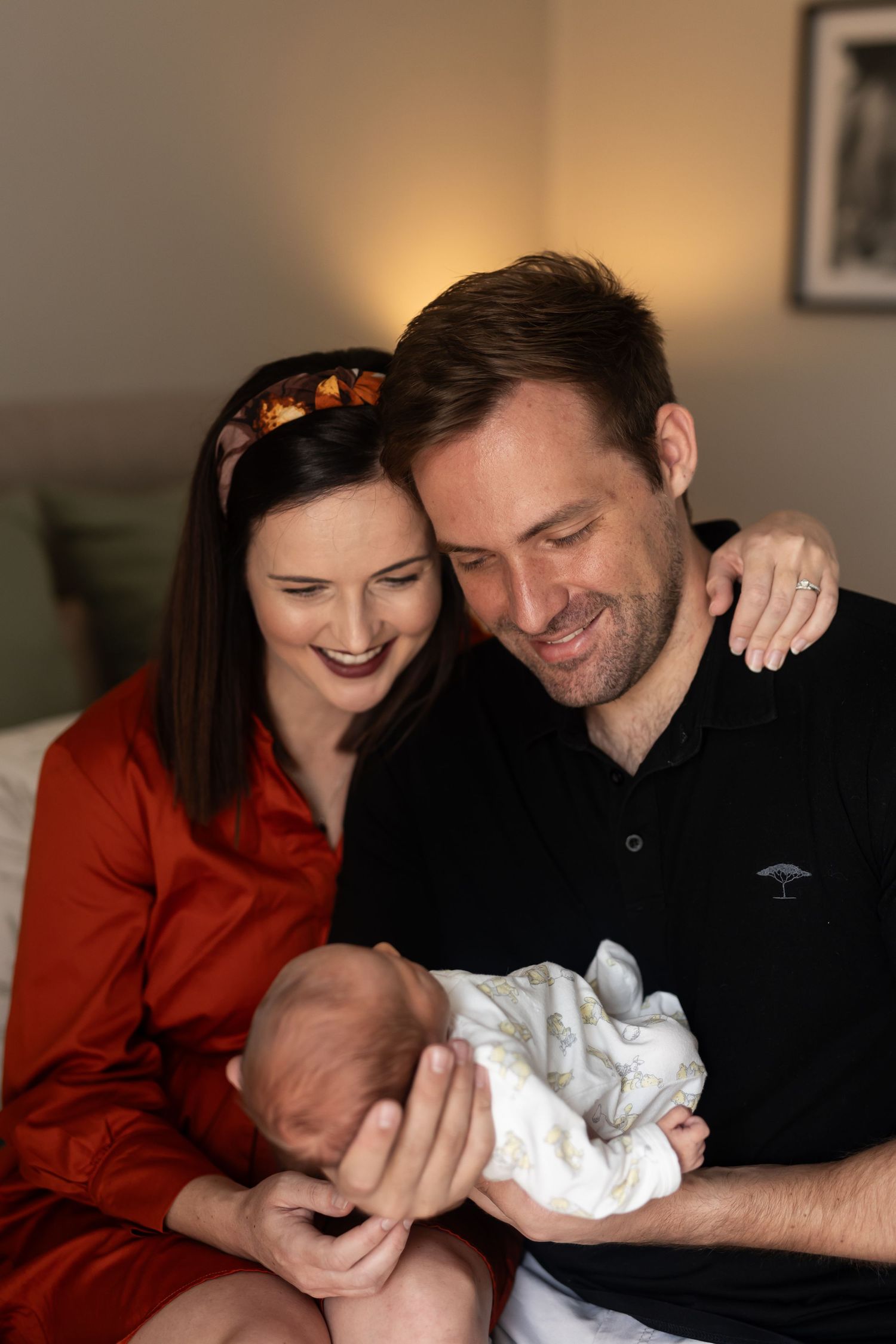 A couple sharing a tender moment while holding their newborn baby wrapped in a white blanket.
