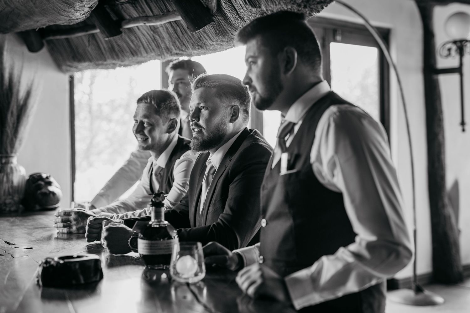 Vintage black and white photo showing three men in formal attire gathered at a bar counter.