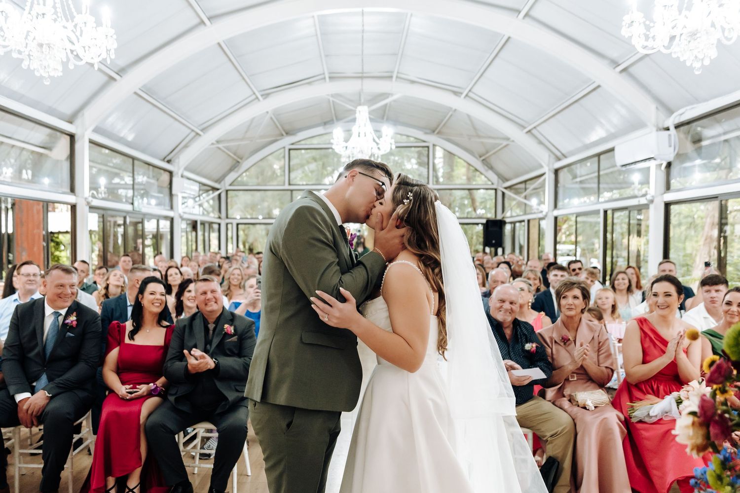 A joyful wedding ceremony moment in a light-filled conservatory surrounded by guests.
