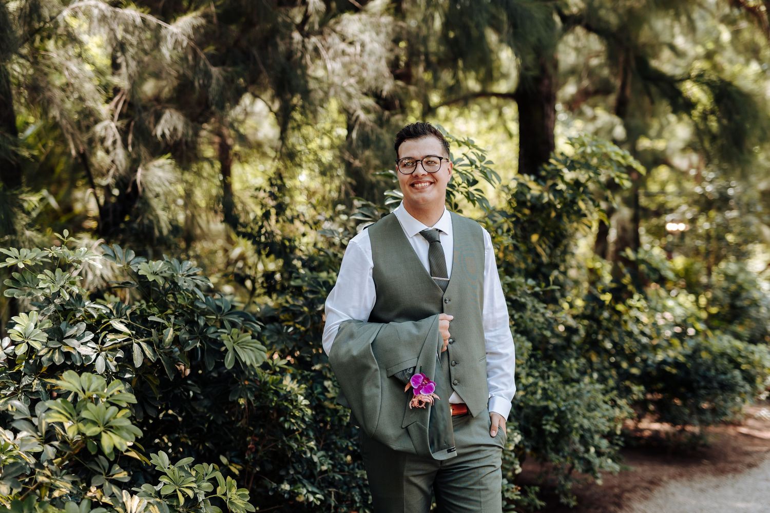 A couple in formal wedding attire poses together in a lush garden setting with natural lighting and greenery.