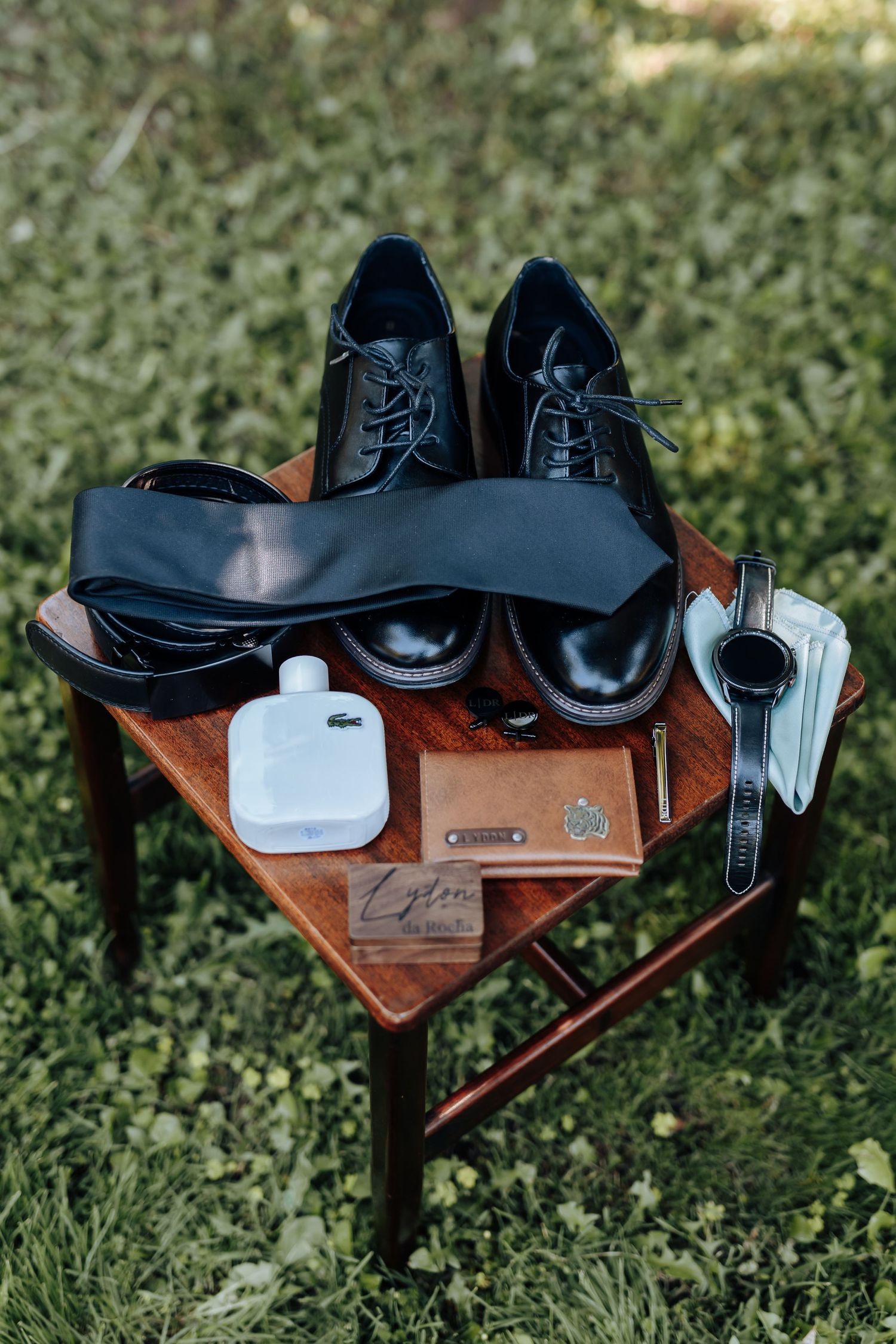Black dress shoes and accessories arranged on a wooden stand against green grass background.