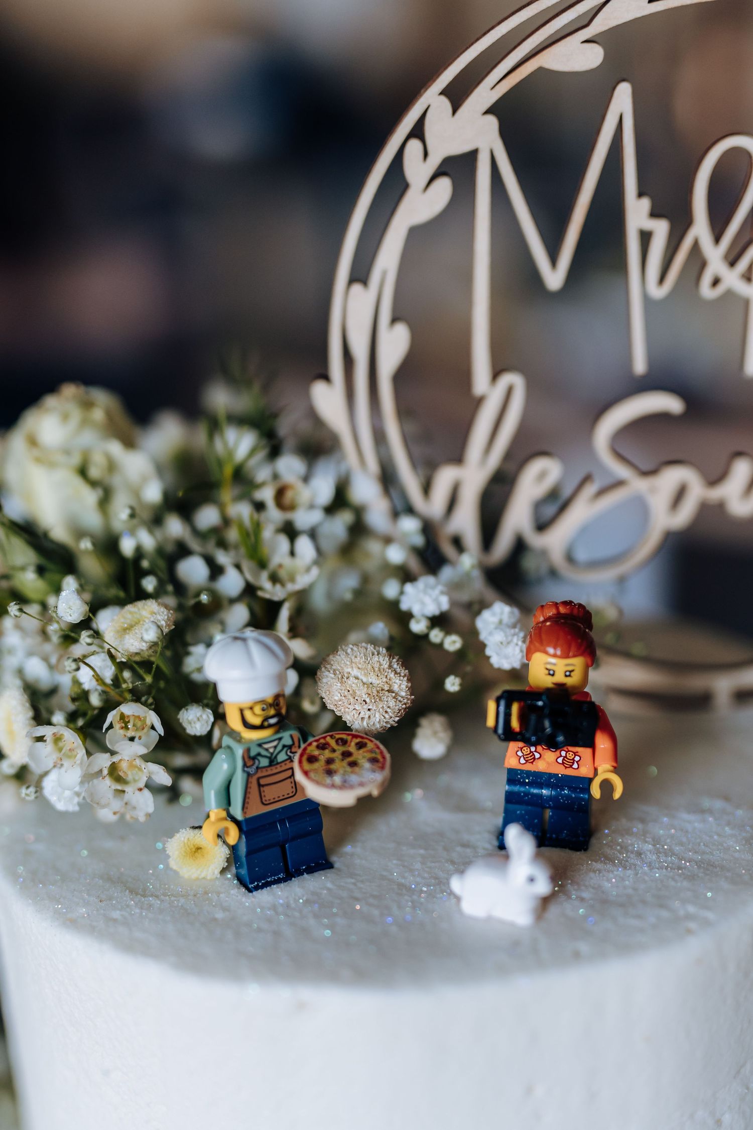 Small LEGO minifigures arranged on a white cake with delicate white flowers as wedding cake decorations.