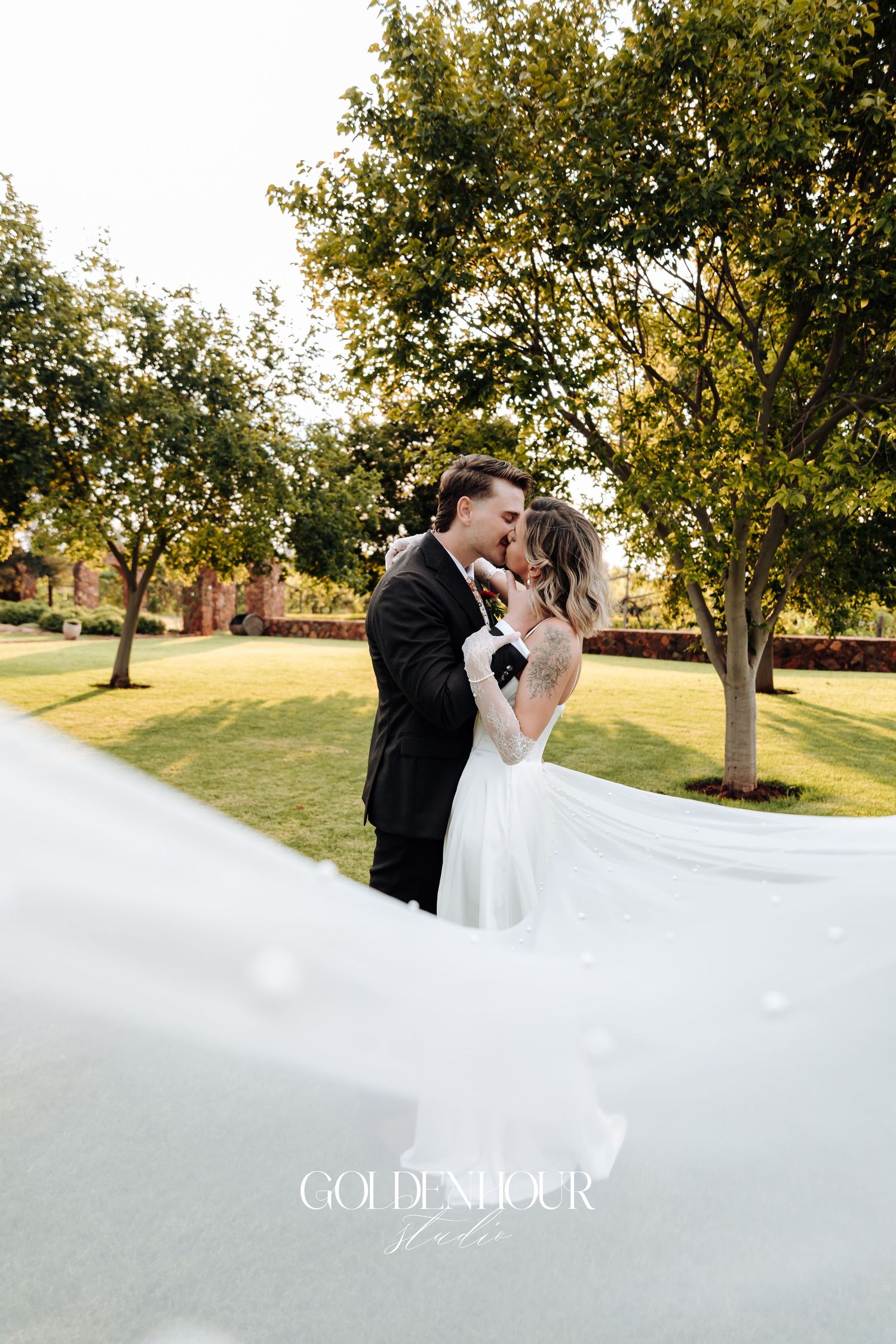 Romantic wedding portrait with flowing veil in an outdoor garden setting.