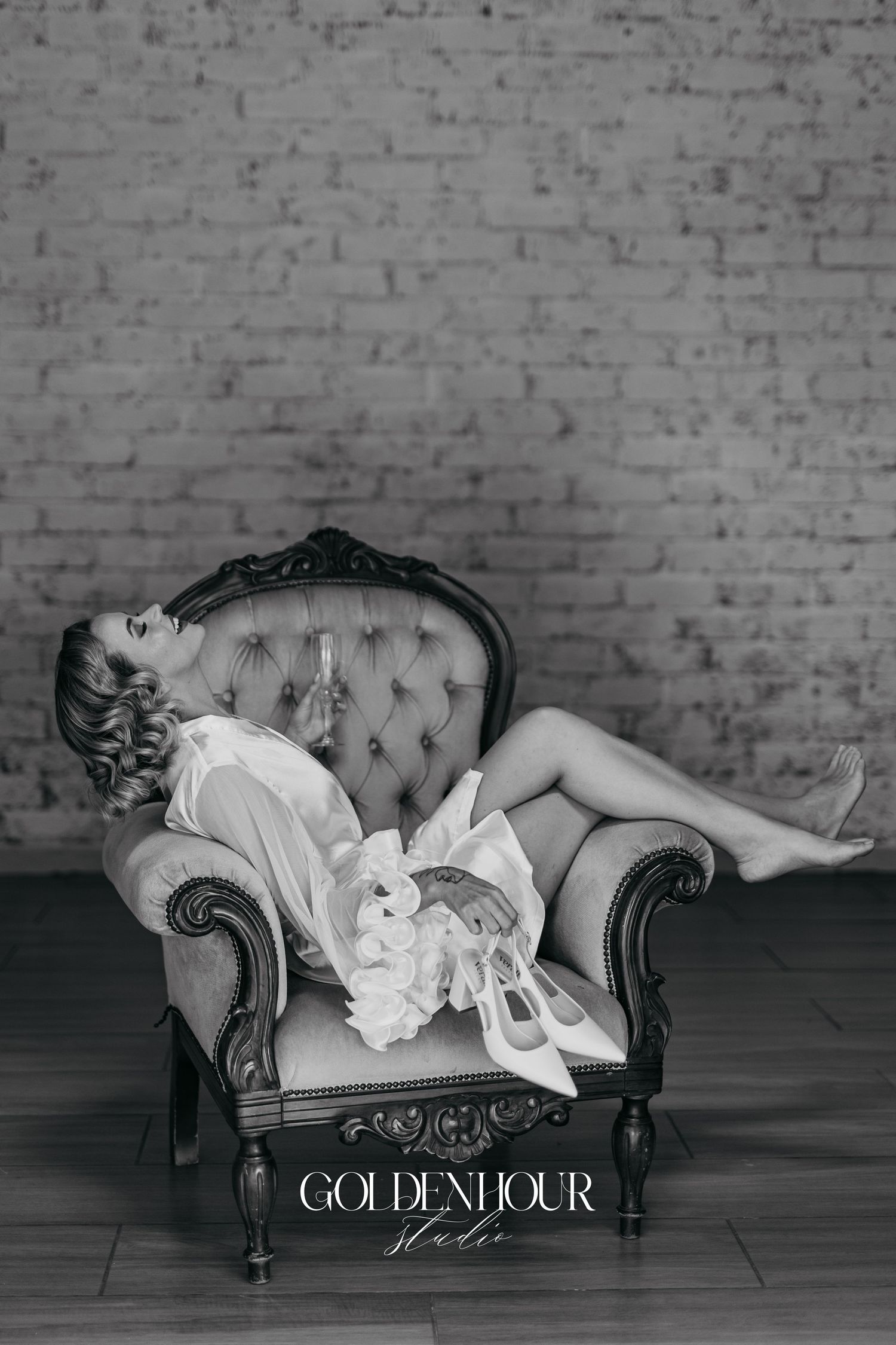 Artistic black and white photo of a vintage tufted chaise lounge in an industrial brick setting.
