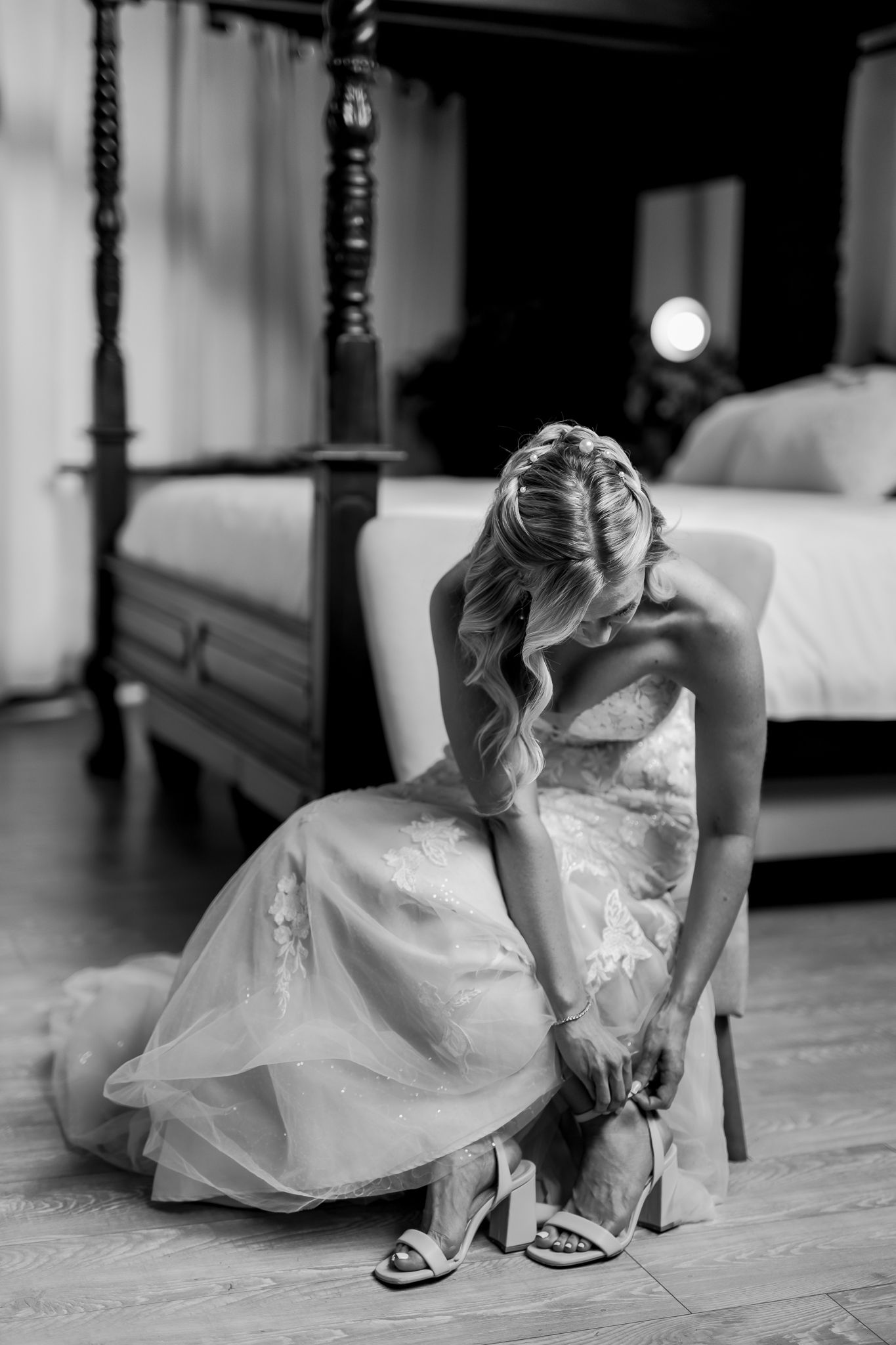 Black and white photo of bride adjusting her shoe before wedding ceremony.