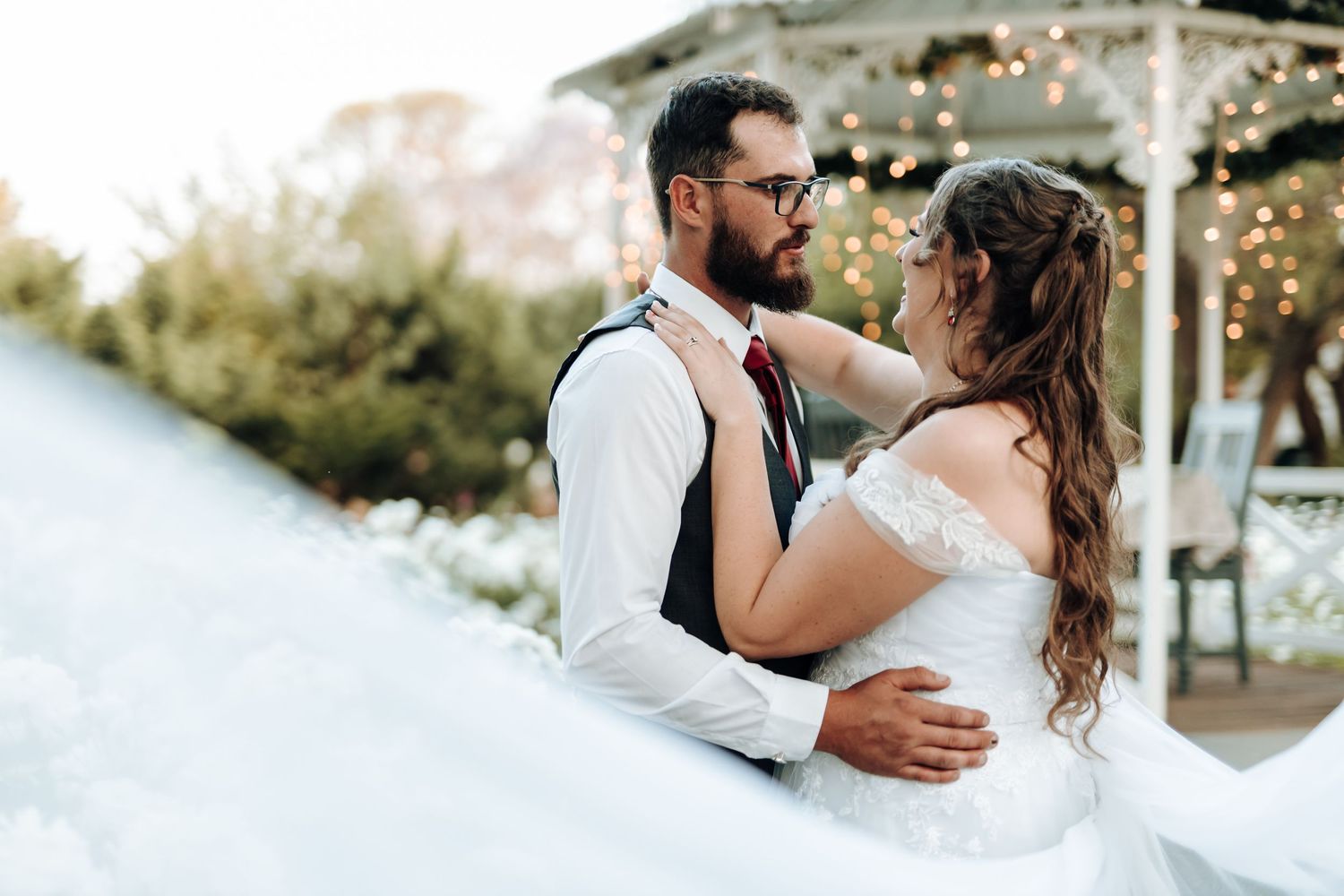 Wedding couple embracing near a lit gazebo at dusk.