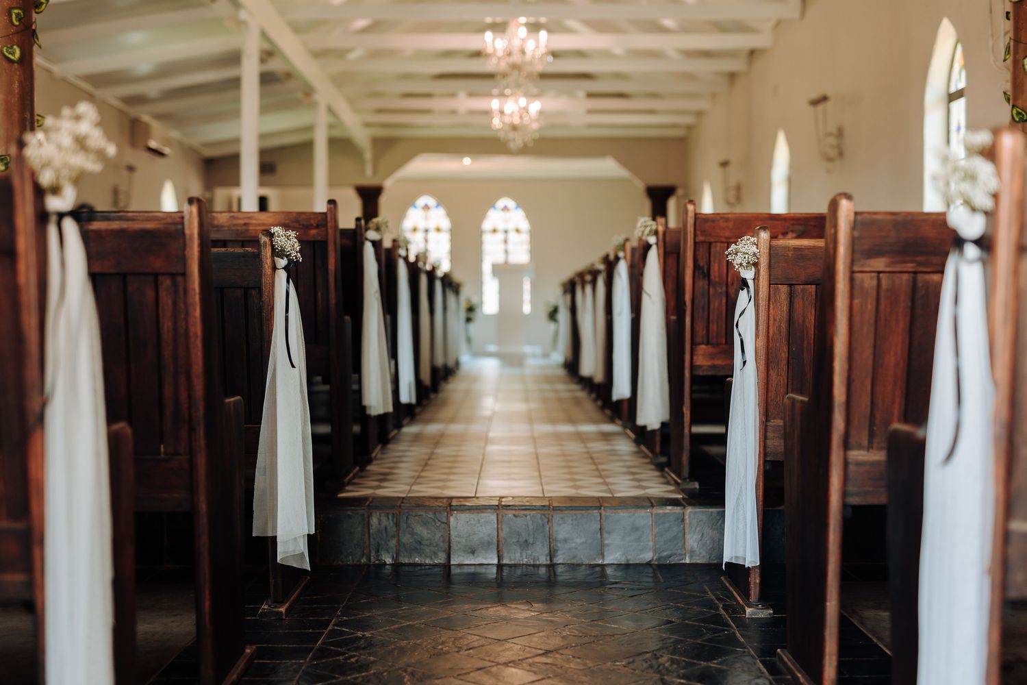 Long church aisle with wooden pews decorated with white fabric and natural light streaming in.