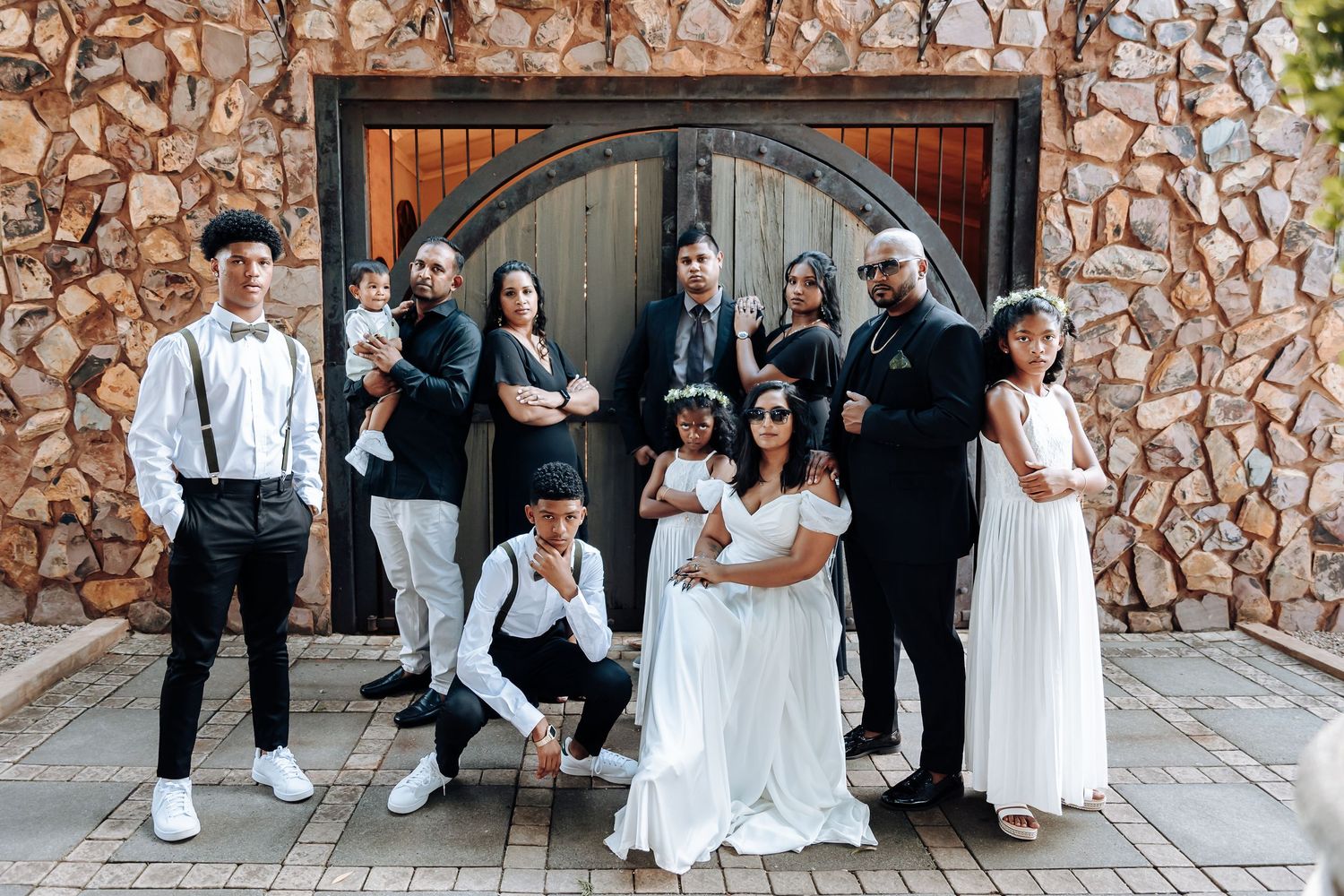Wedding party poses together in front of rustic stone wall and wooden door.