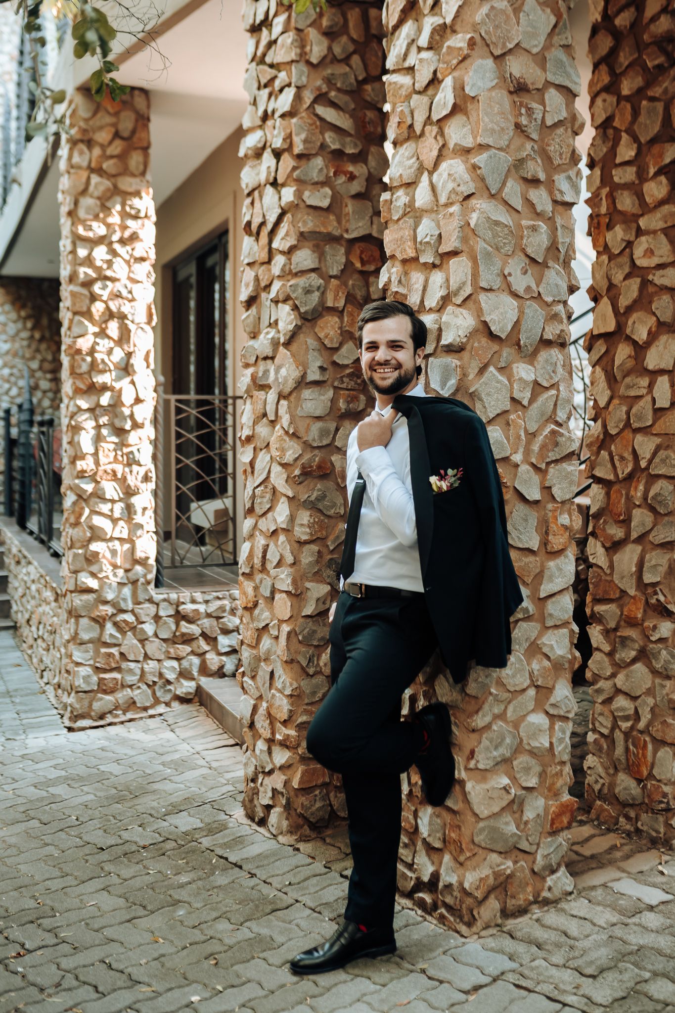 Formal portrait against stone pillars with rustic architecture and brick walkway.