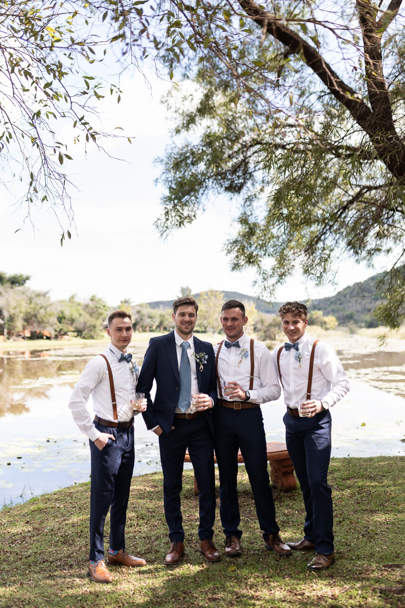 Wedding party in coordinated navy and white attire posing by lake.